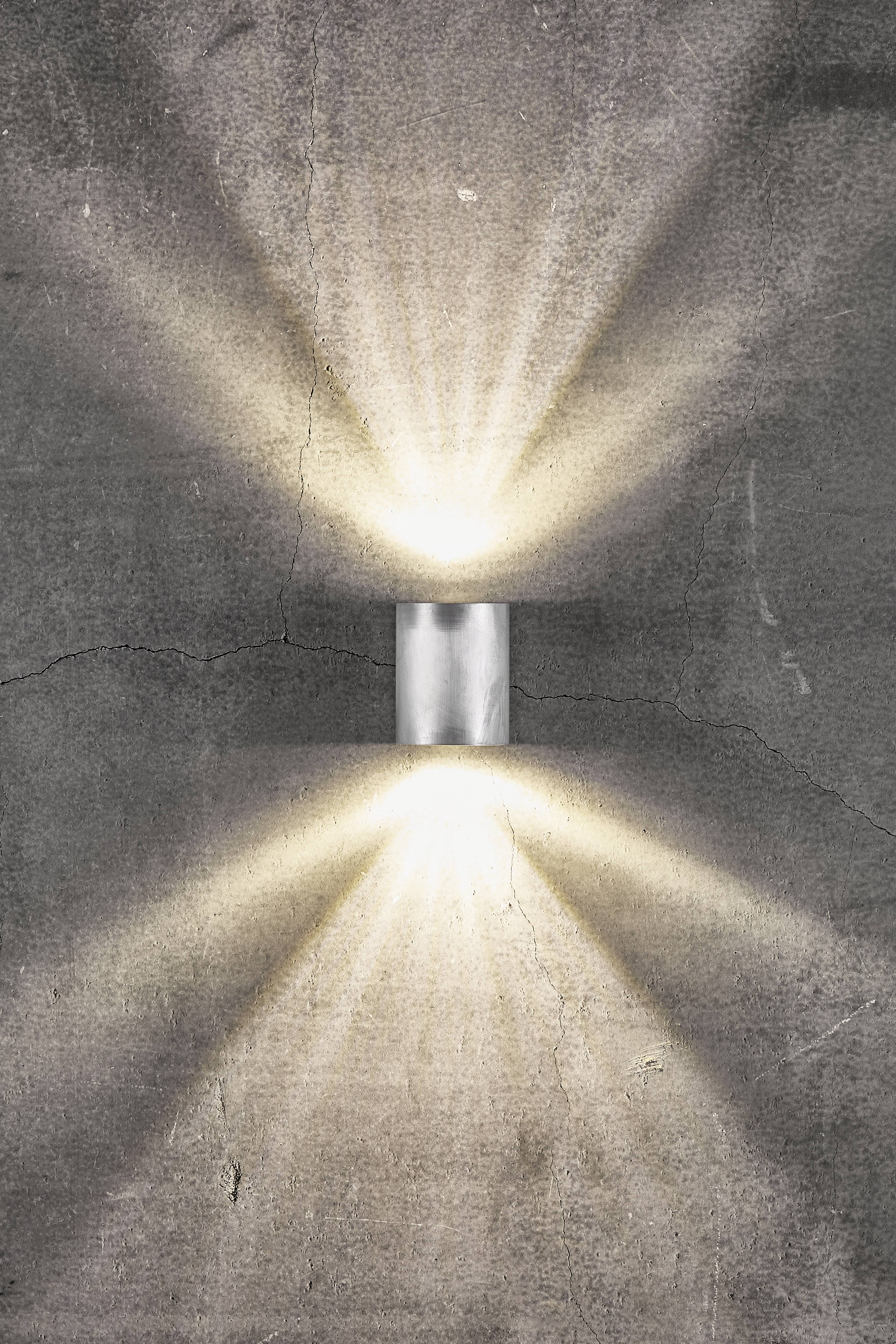 Wall light on a grey wall, casting light upwards and downwards, creating ray-like patterns.