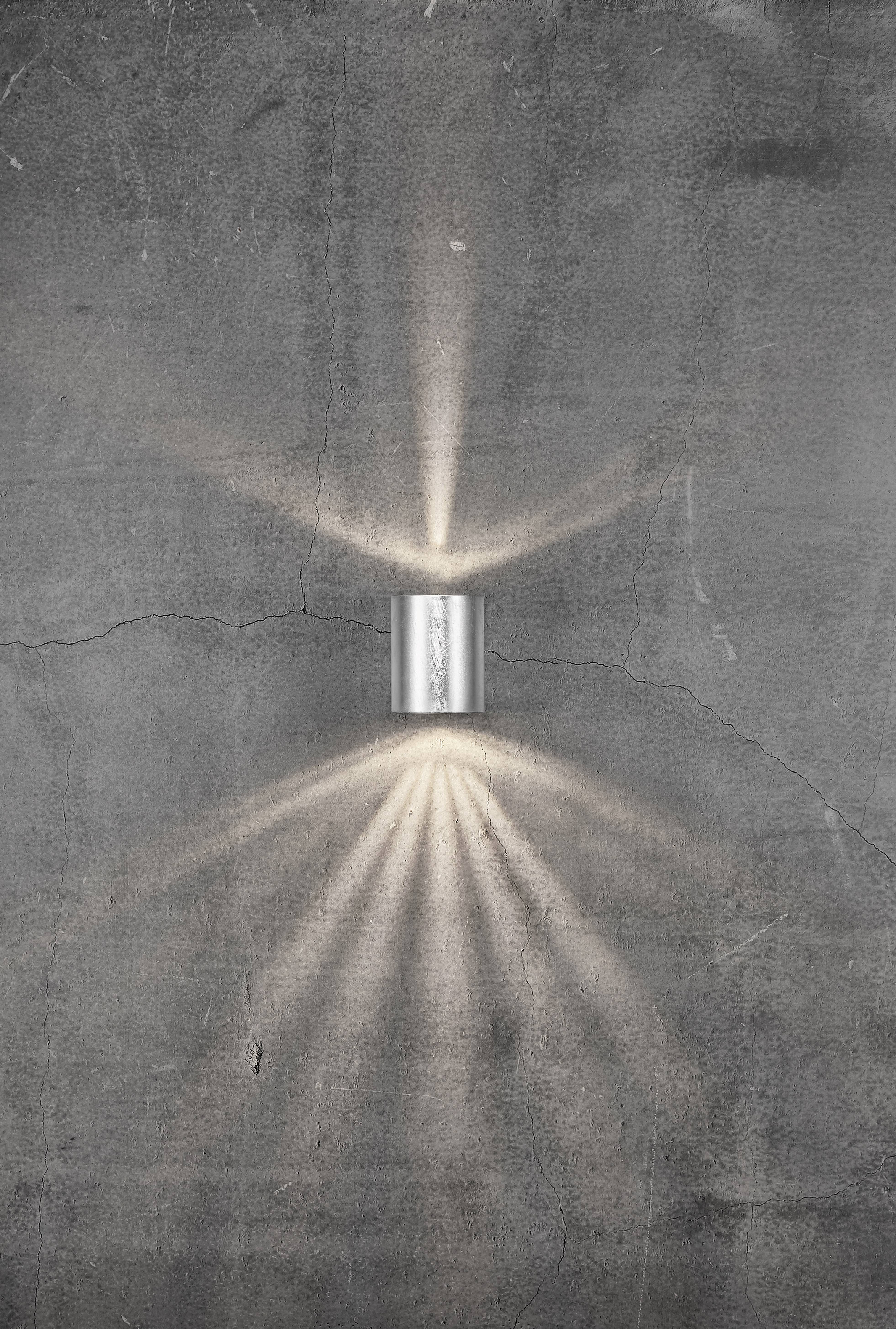 Wall light on a grey concrete wall creates a radiant light pattern extending upwards and downwards.