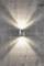 Wall light mounted on a grey concrete wall shines upwards and downwards, creating radiant light patterns on the wall surface.