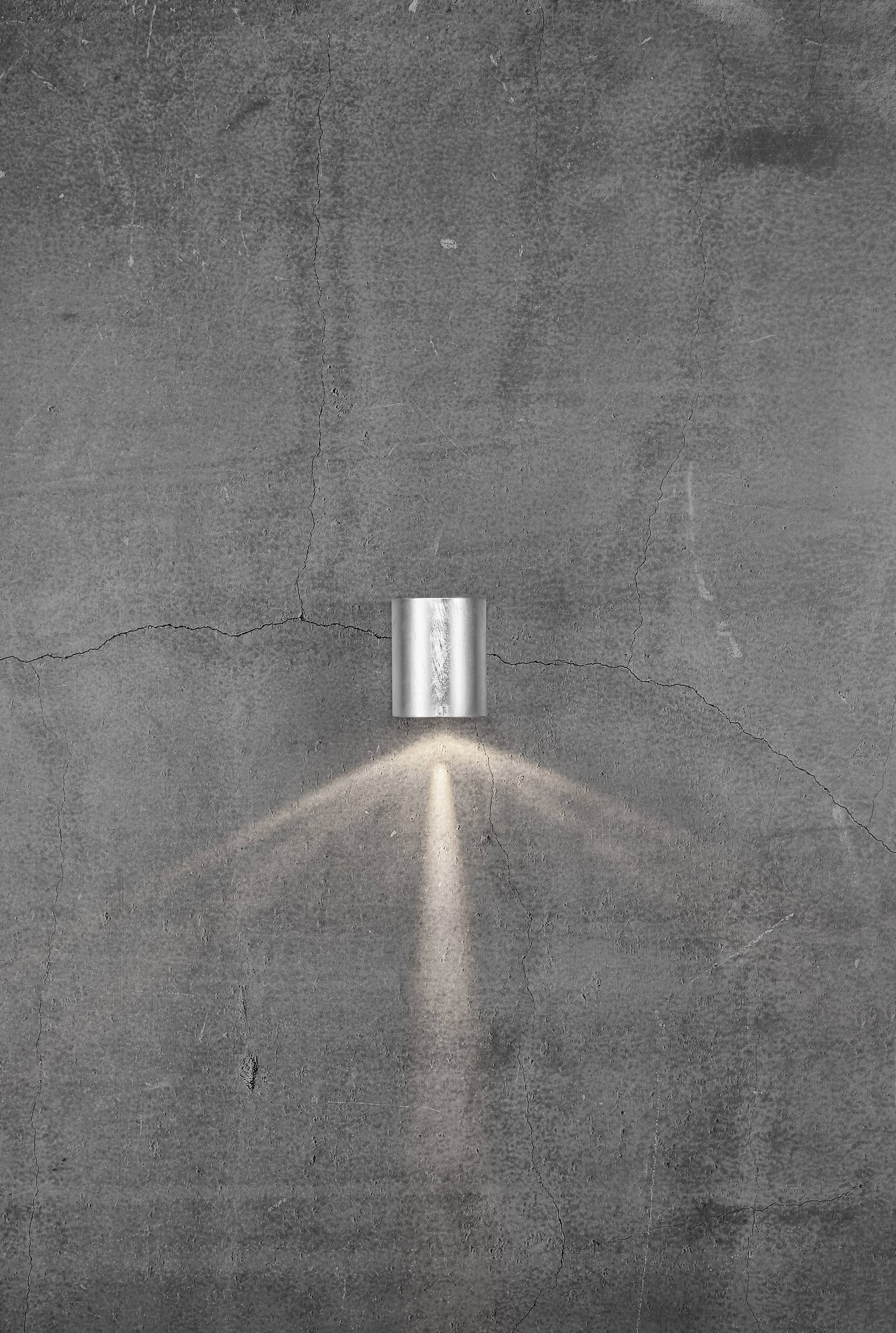 A single cylindrical lamp illuminates a grey, weathered concrete wall, casting a conical beam of light.