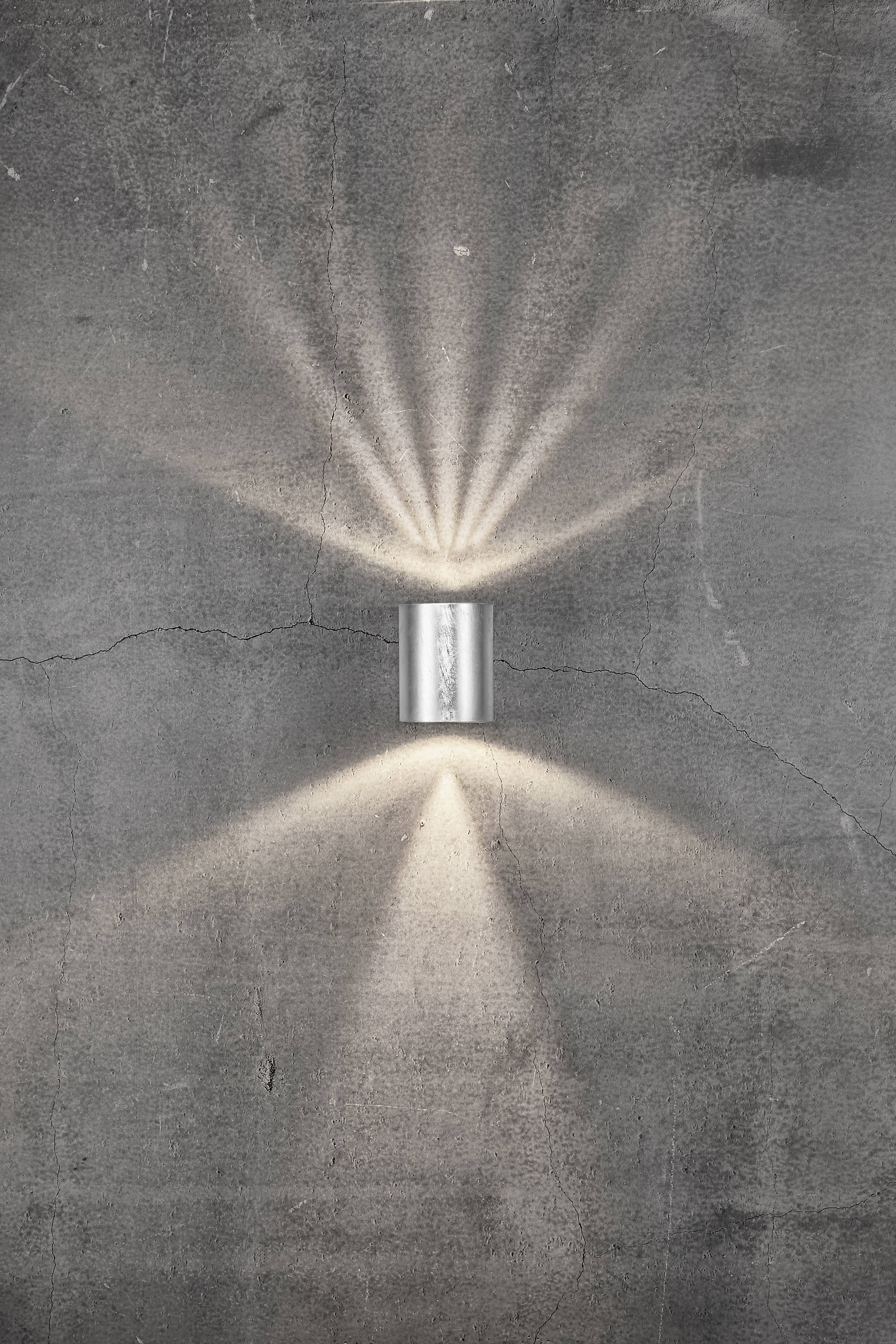 Wall light mounted on a concrete wall, casting light upwards and downwards to create a decorative lighting effect.