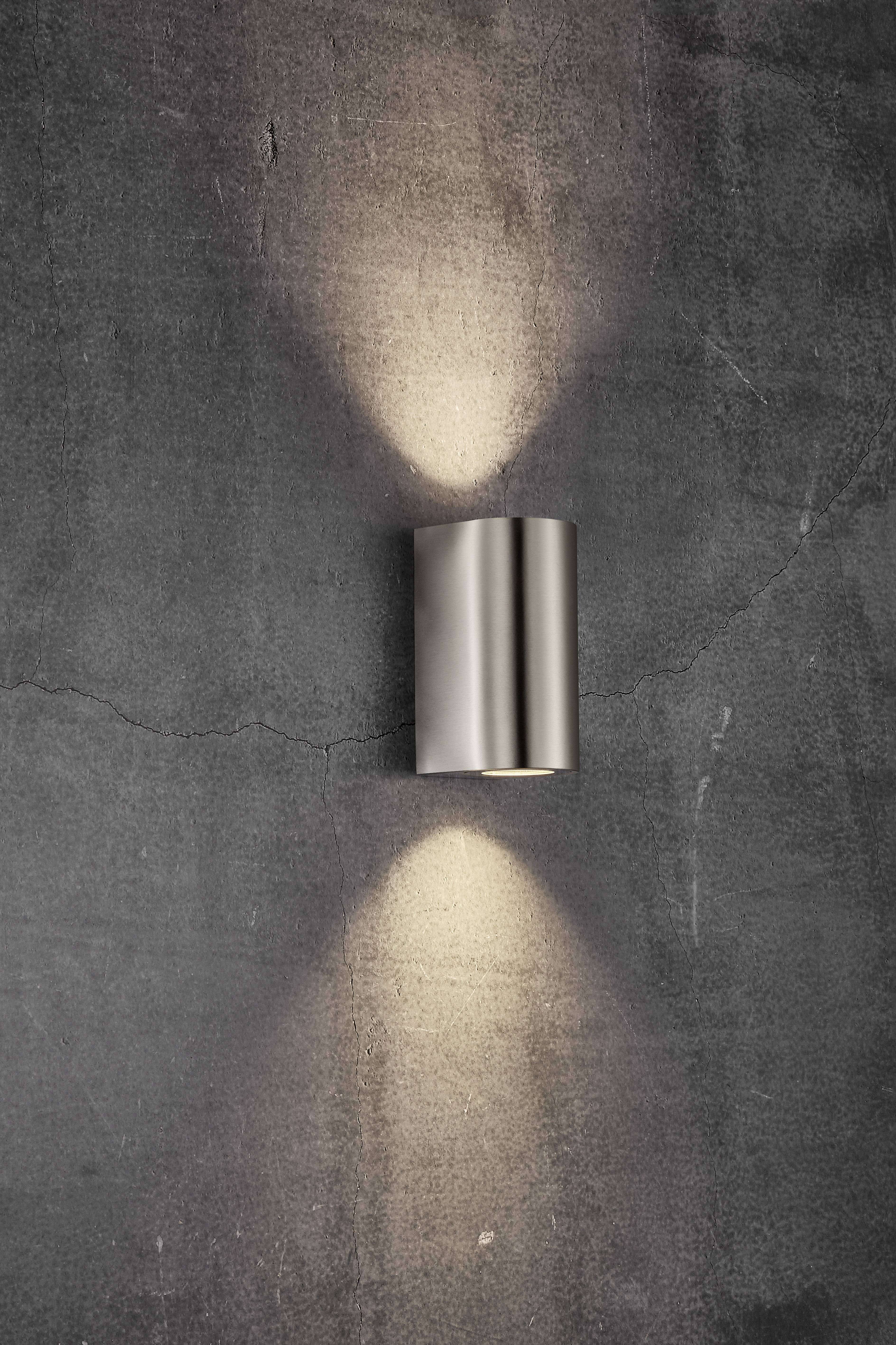 Wall light in silver, illuminating upwards and downwards against a grey concrete wall, simple modern lighting.