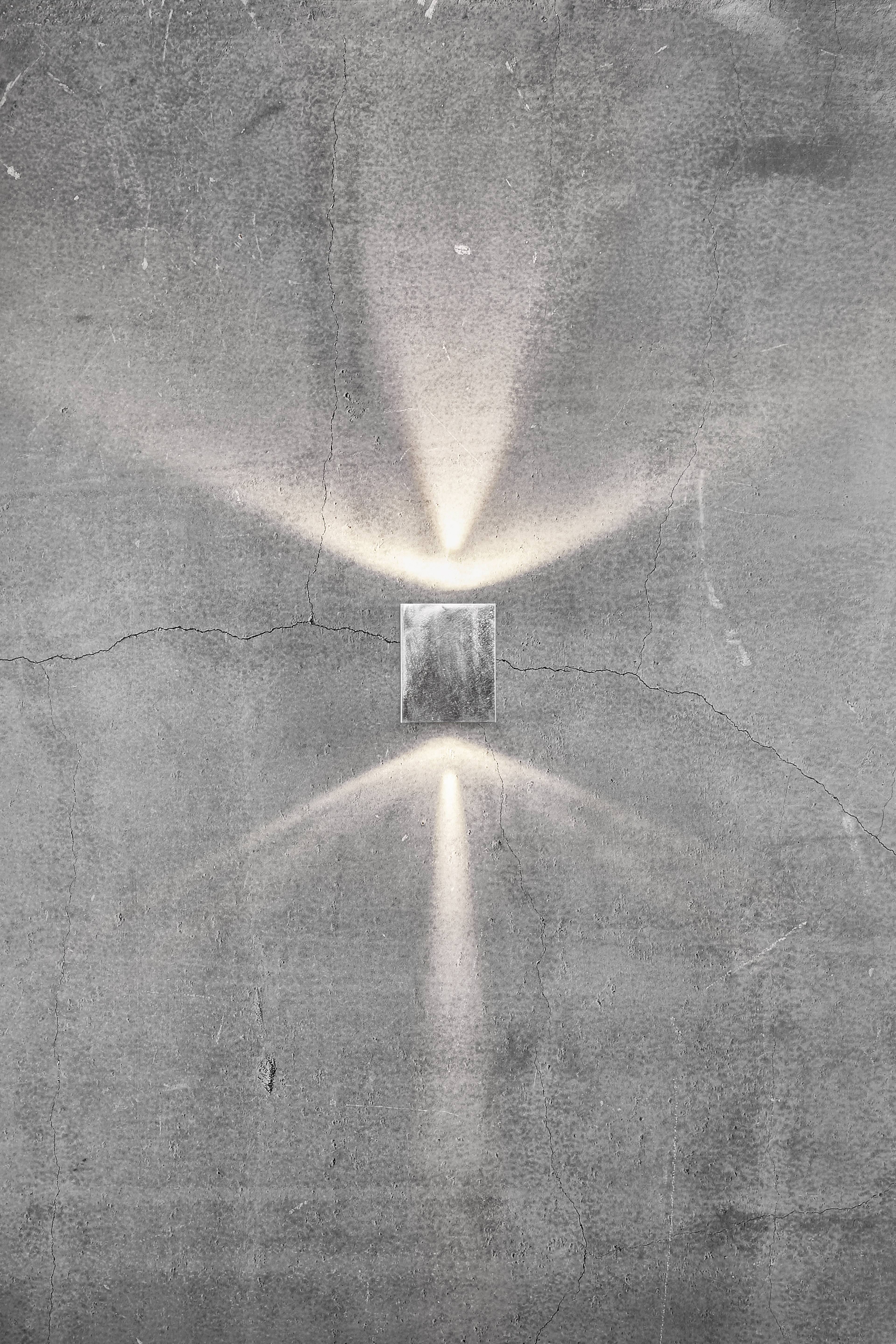 A minimalist light fixture on a concrete wall emits light rays upwards and downwards, creating a cross pattern.