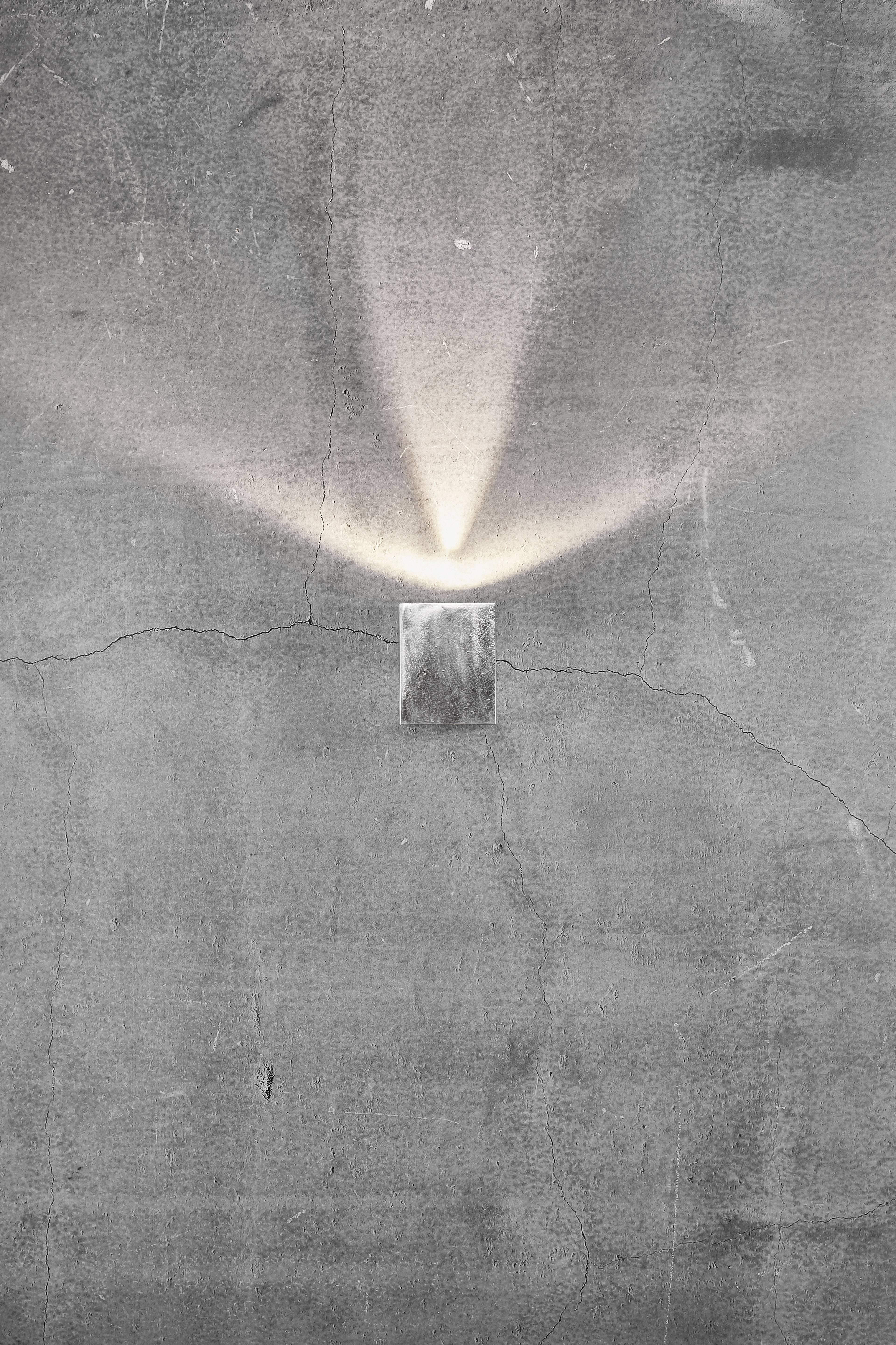 Wall light on concrete wall casts triangular light pattern upwards.