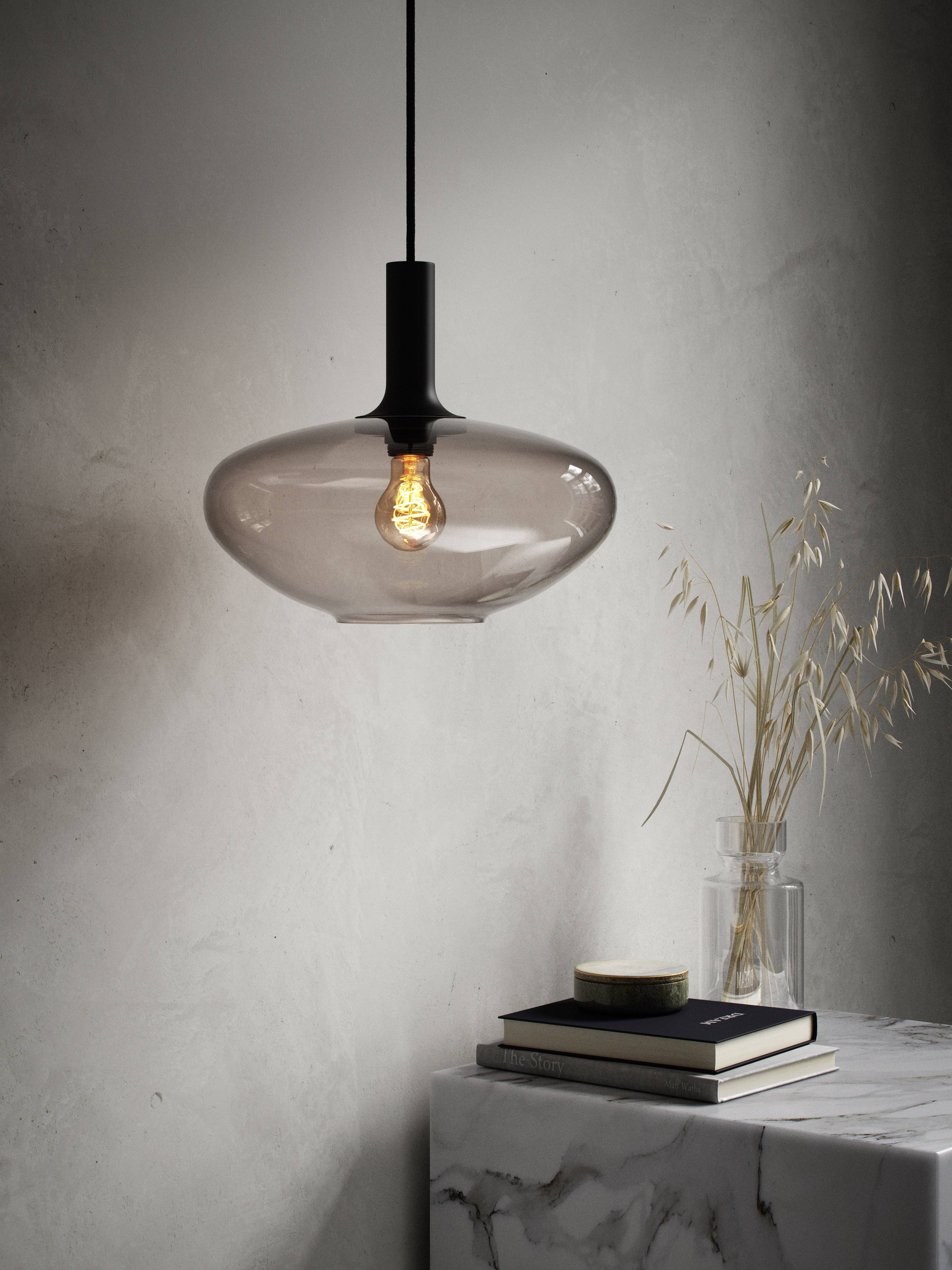 An elegant, transparent pendant light with its illumination switched on hangs above a marble table, where books and a vase are placed.