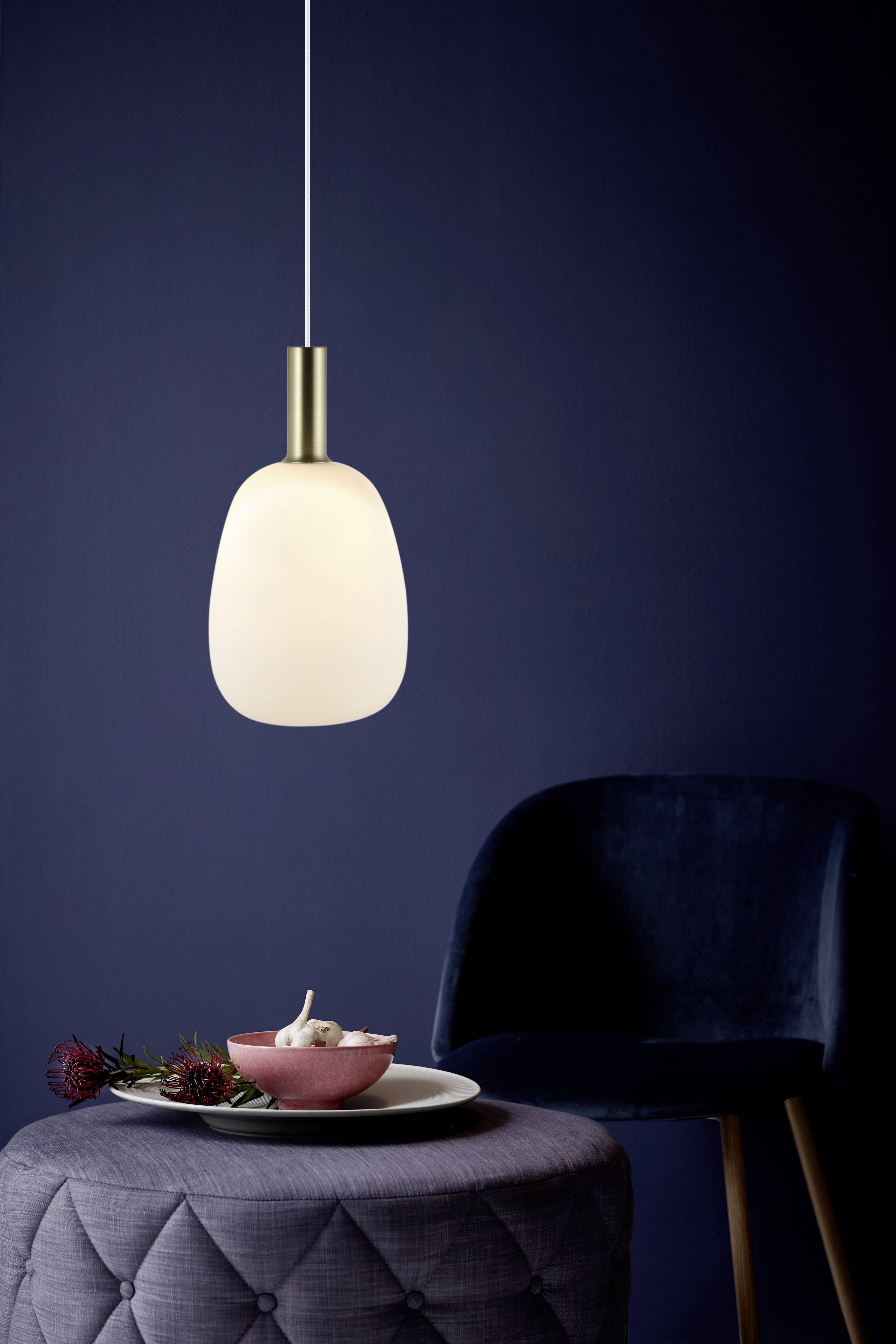 A hanging pendant light illuminates a round table with a bowl and flowers. In the background stands a dark blue chair.