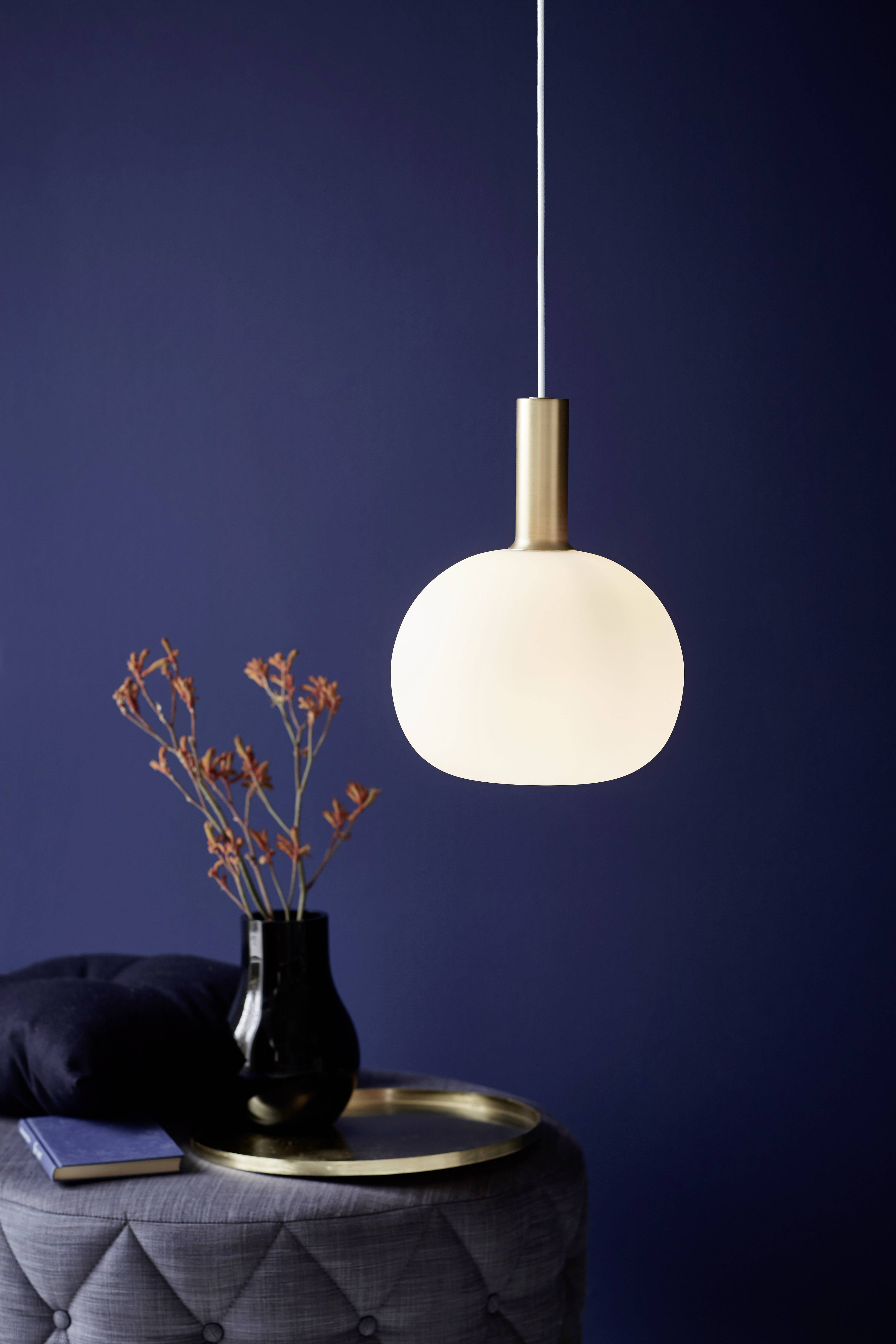 A hanging, round lamp illuminates beside a table with a black vase and orange flowers. The background is dark blue.