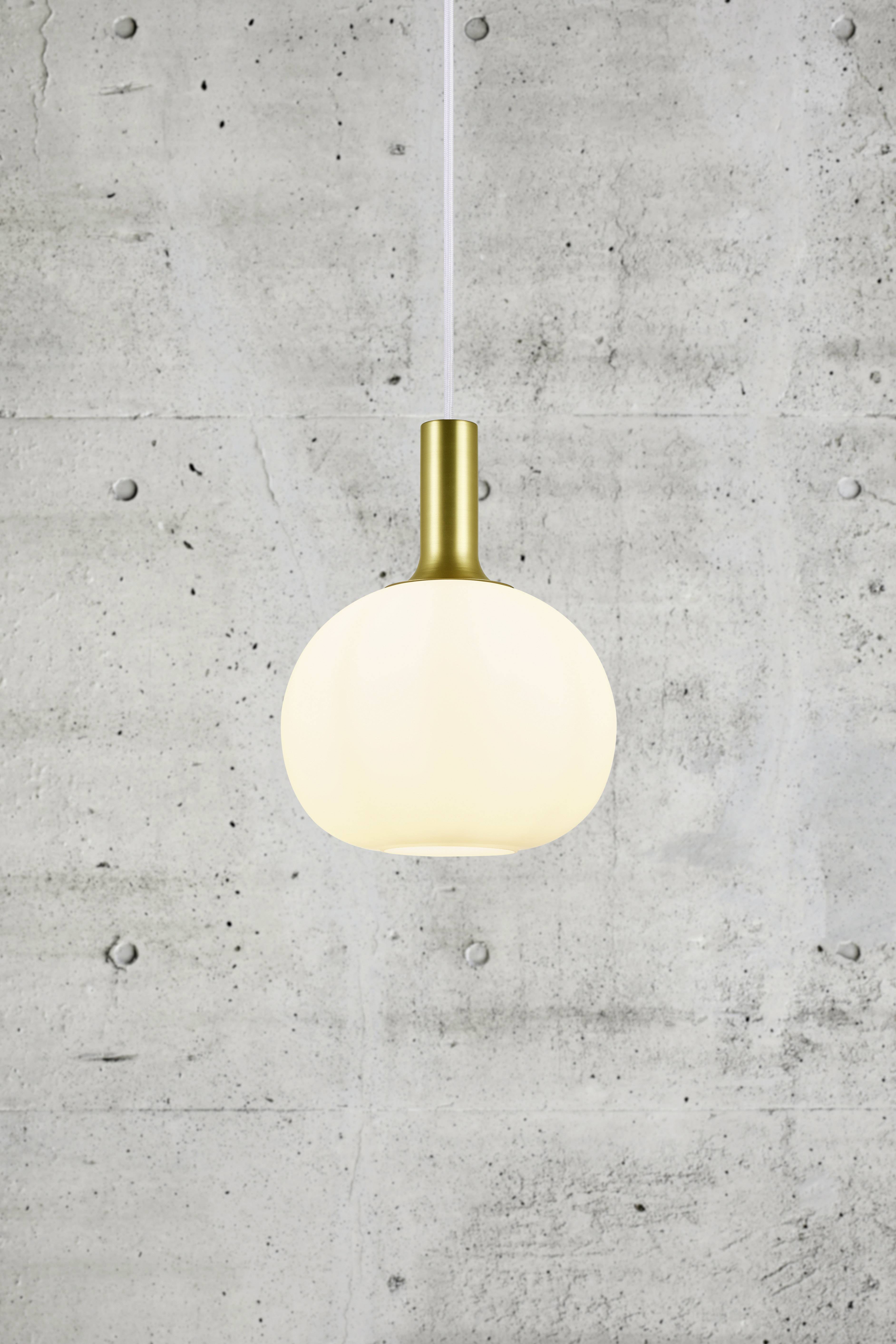 Modern hanging light with a round, matte shade and gold fitting against a concrete wall. Perfect for minimalist interior design.