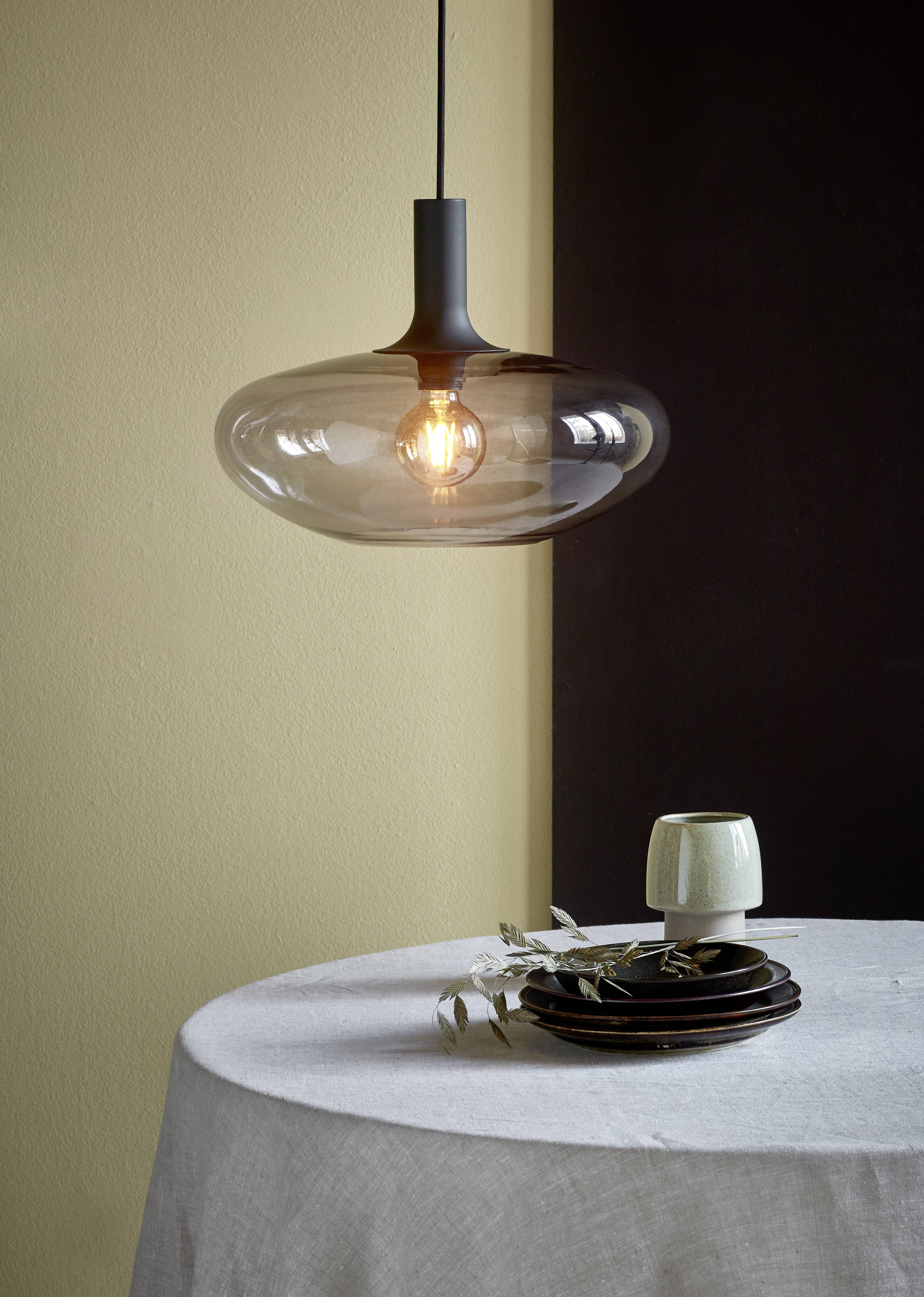 A modern light bulb hangs over a laid table with a cup and ceramic plates on a tablecloth.
