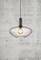 Modern pendant light with transparent glass and visible bulb, hanging in front of a grey concrete wall.