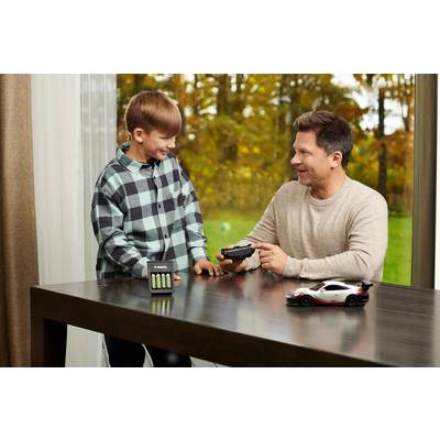 A boy and a man are playing with a remote-controlled car at the table. The boy is laughing while the man drives the car. Outside, it's autumn.