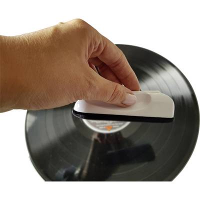 A hand is cleaning a vinyl record with a white brush.