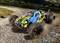 A remote-controlled car with a colourful design races quickly along a gravel path, kicking up dust. The background shows a landscape.