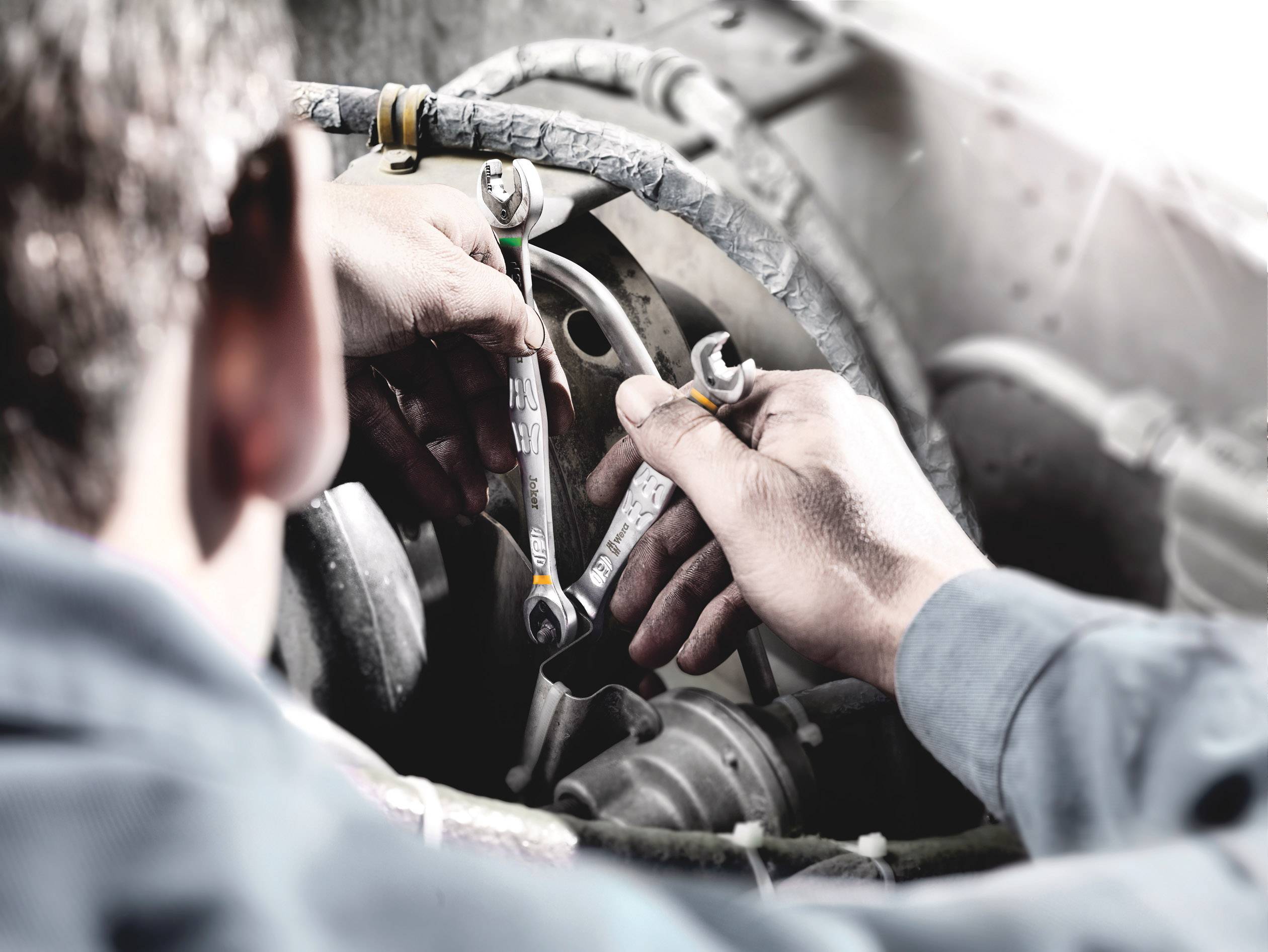 A person is repairing an engine, holding two spanners and working on a cable harness inside a machine.