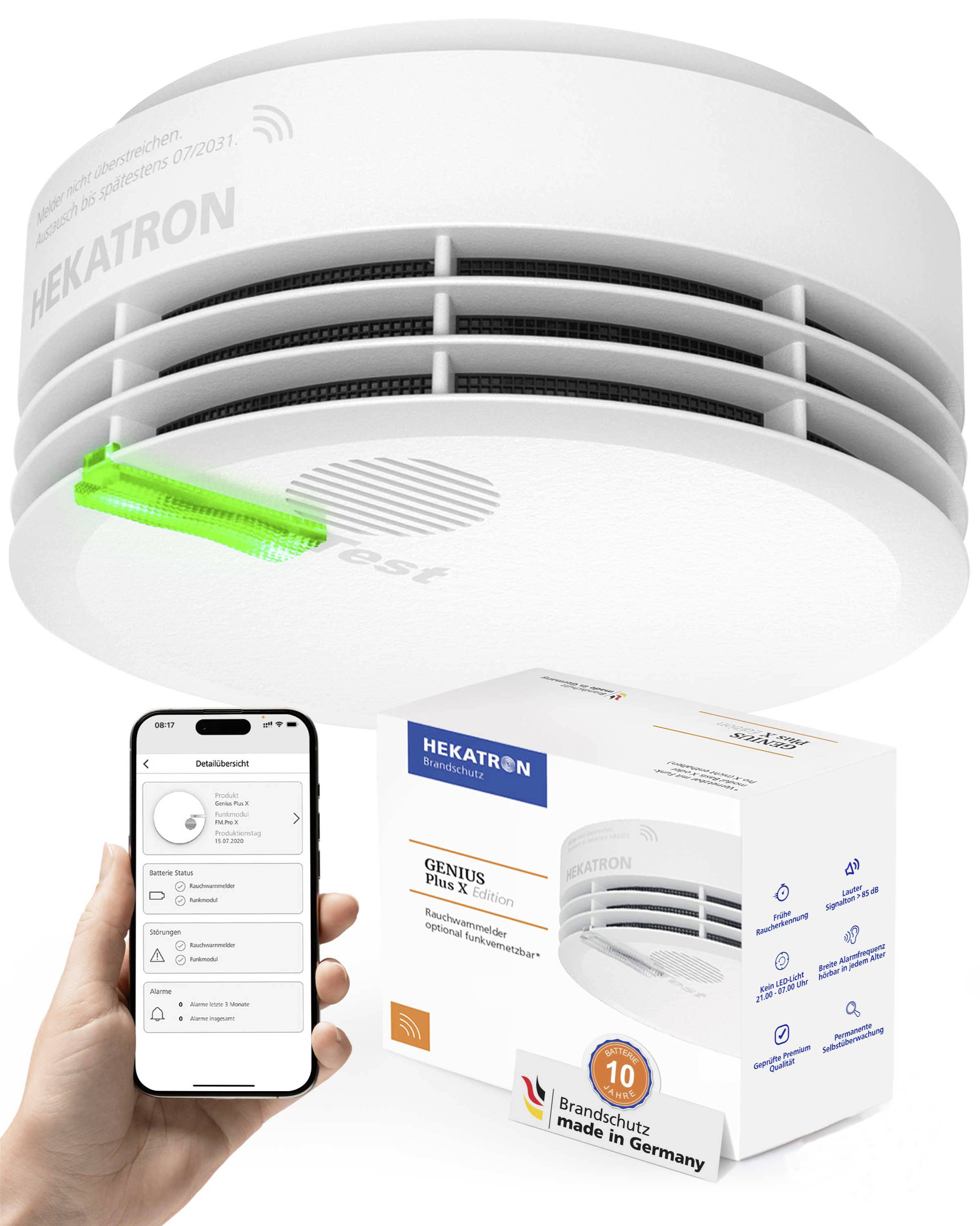 A smoke detector with a glowing green indicator shows it’s functional. A hand holds a smartphone displaying a connected app interface.