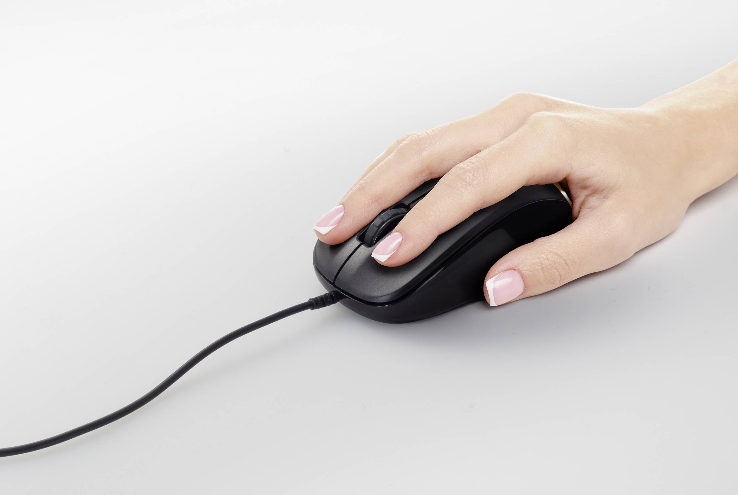 A hand is operating a wired computer mouse on a smooth, light-coloured surface.