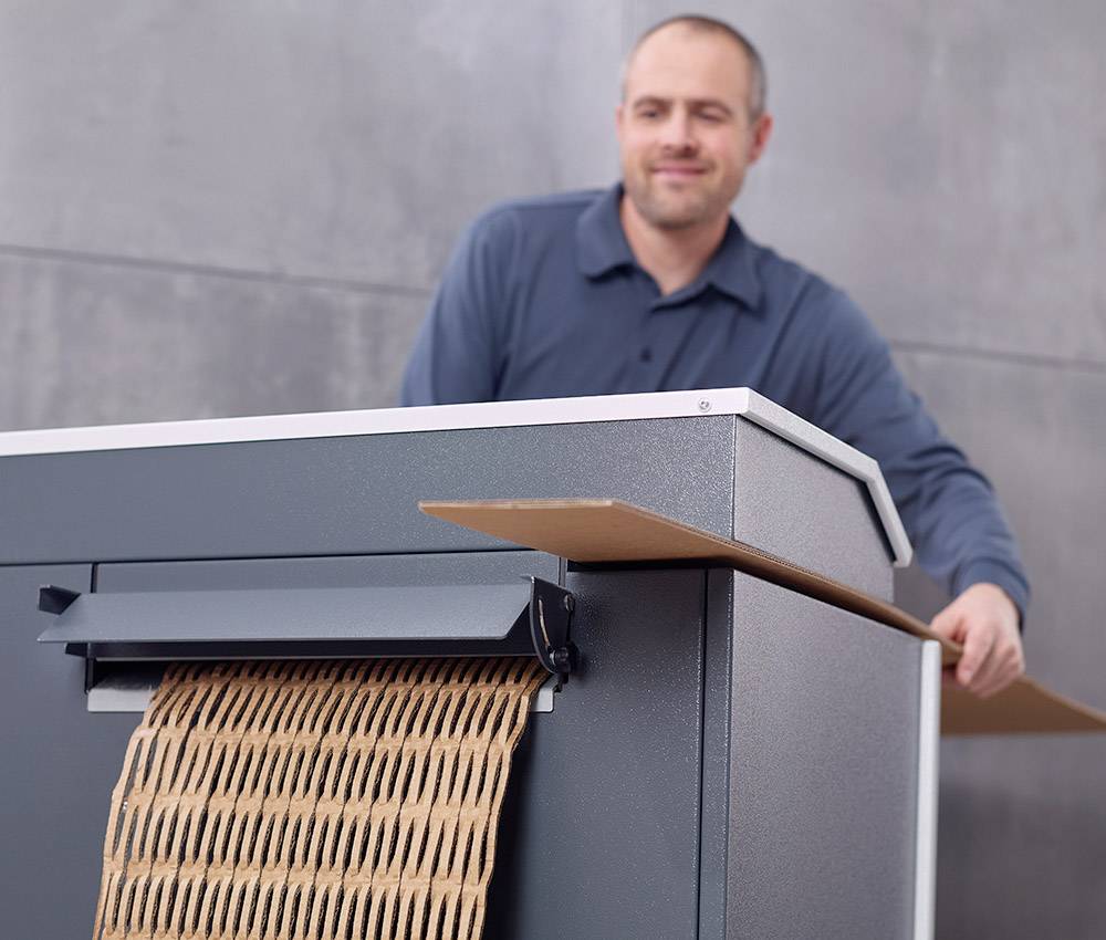A man is using a machine that compresses cardboard into a shredder-like shape.