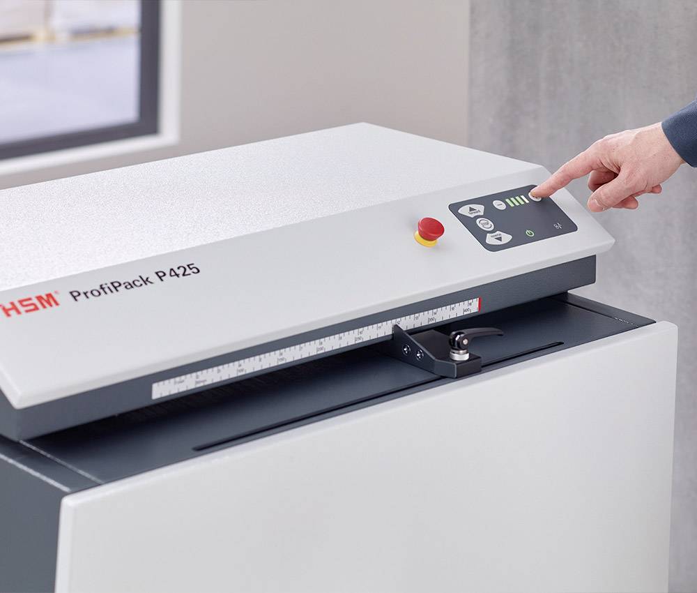 A hand operates a cardboard shredder with buttons and an emergency stop button. The machine is labelled 'ProfiPack P425'.