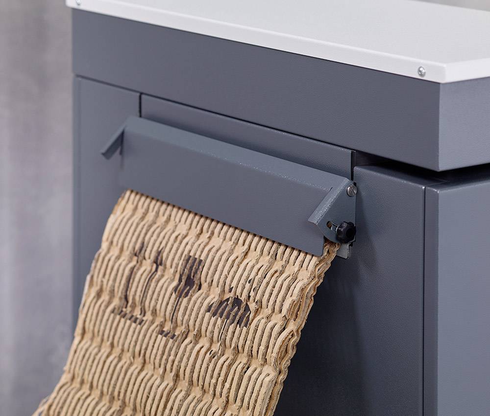 A cardboard box is processed by a machine into a wavy, corrugated structure, presumably for recycling or protection purposes.