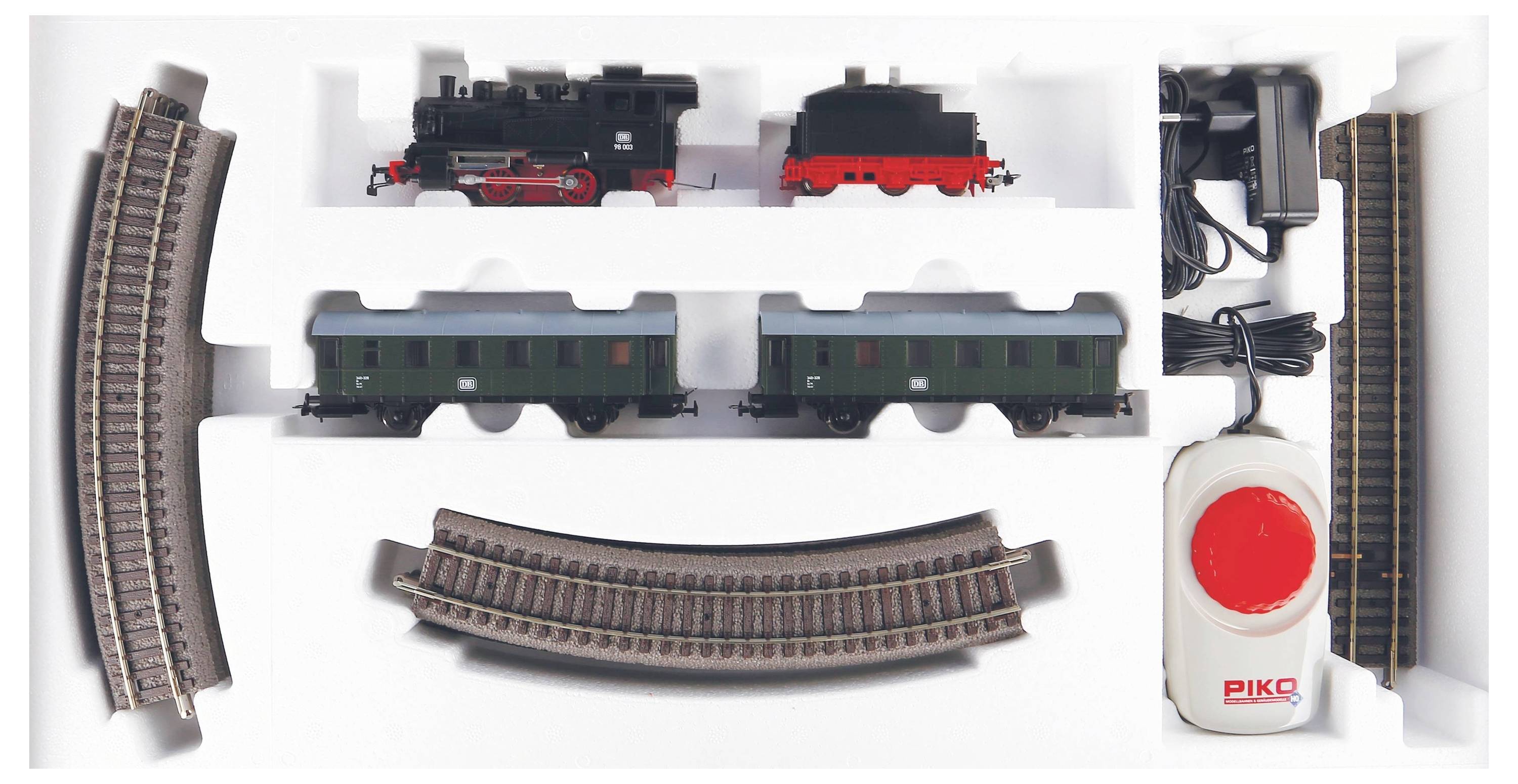Model railway set with steam locomotive, two carriages, curved and straight tracks, and a control unit in white foam packaging.