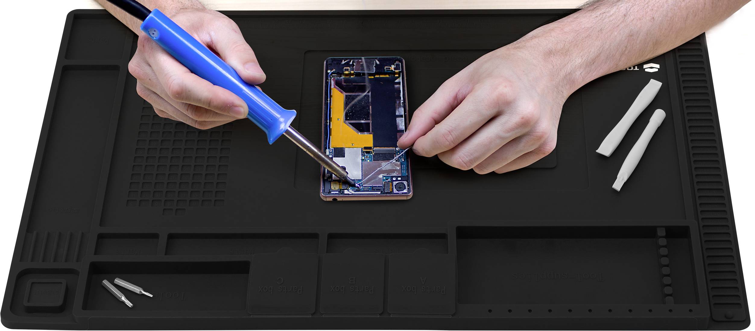 A person is repairing a smartphone on a black work mat with a soldering iron and mobile phone repair tools.