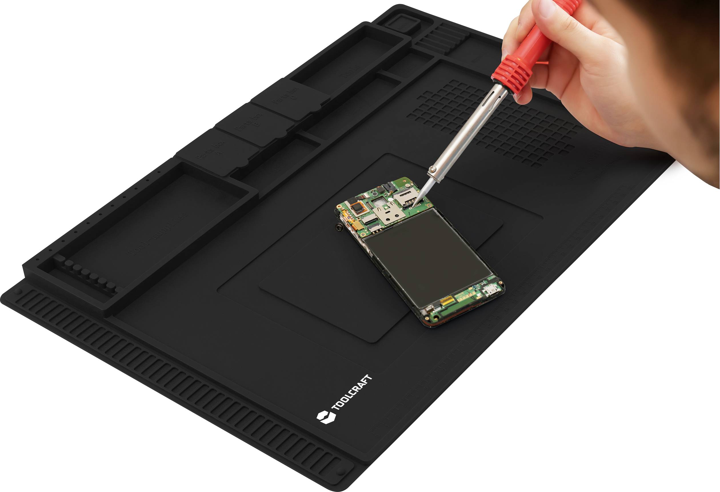 A person is soldering an opened smartphone on a non-slip mat with compartments for tools and parts.