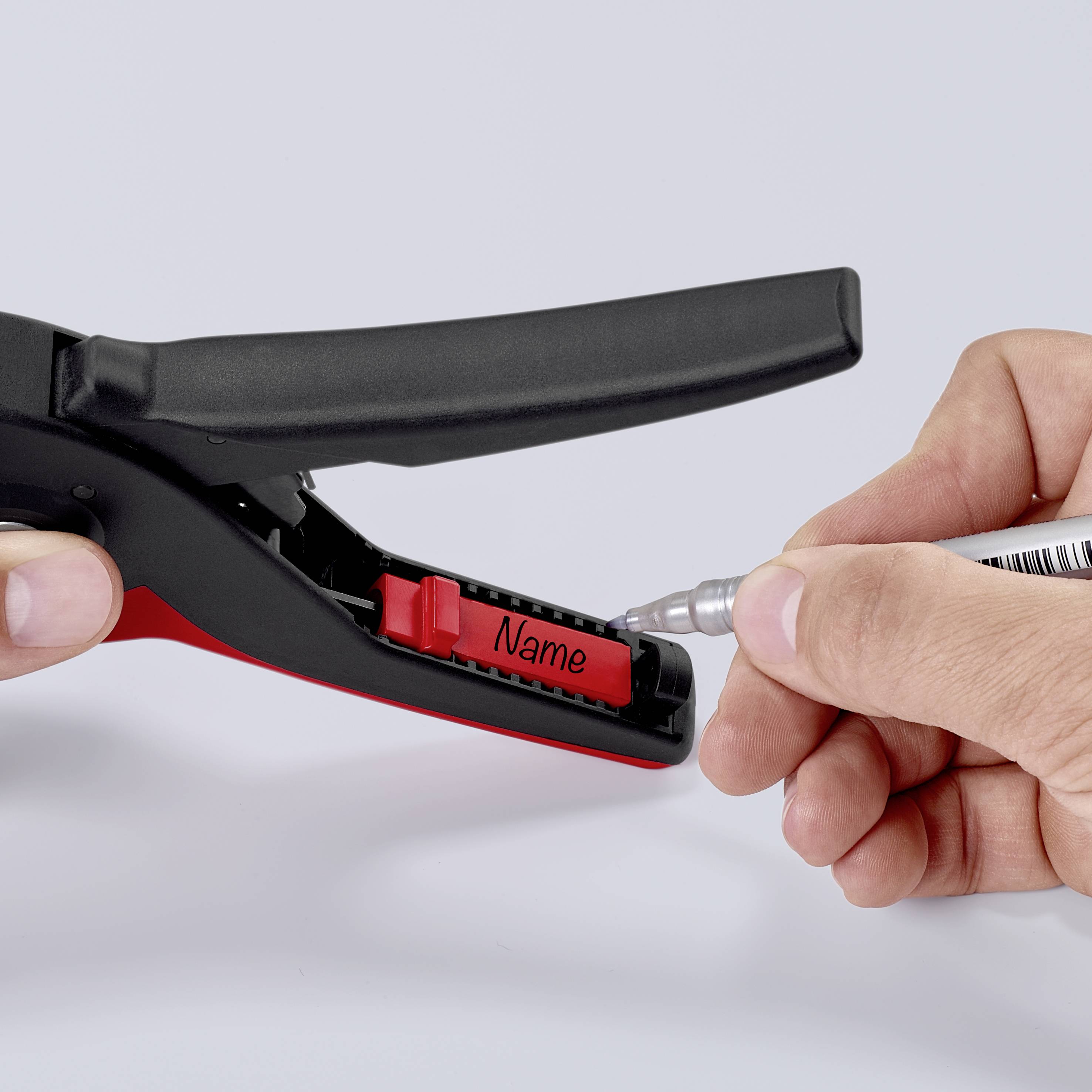 A hand is writing a name on a red name badge attached to a black holder.