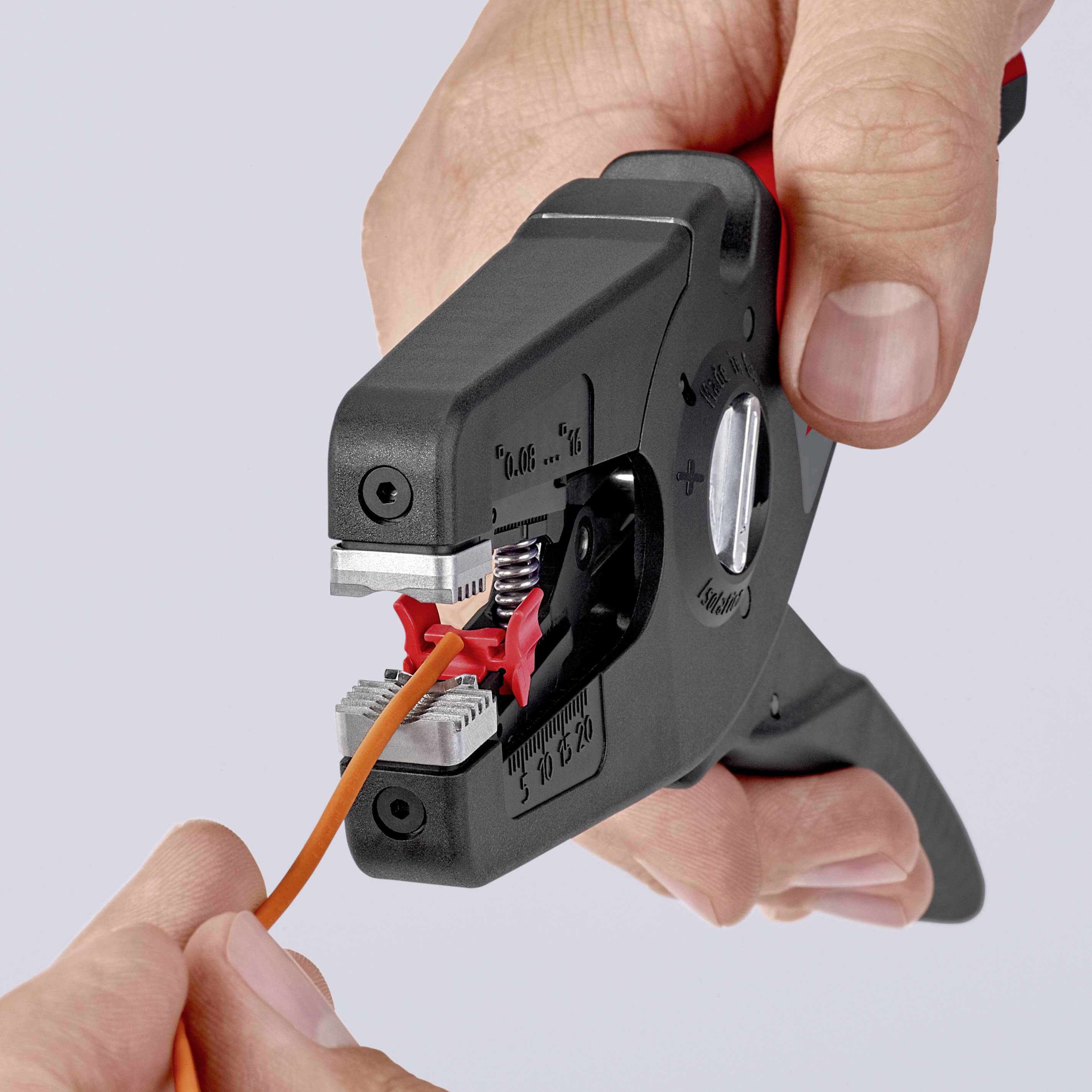 A hand holds an automatic wire stripper precisely stripping an orange cable.