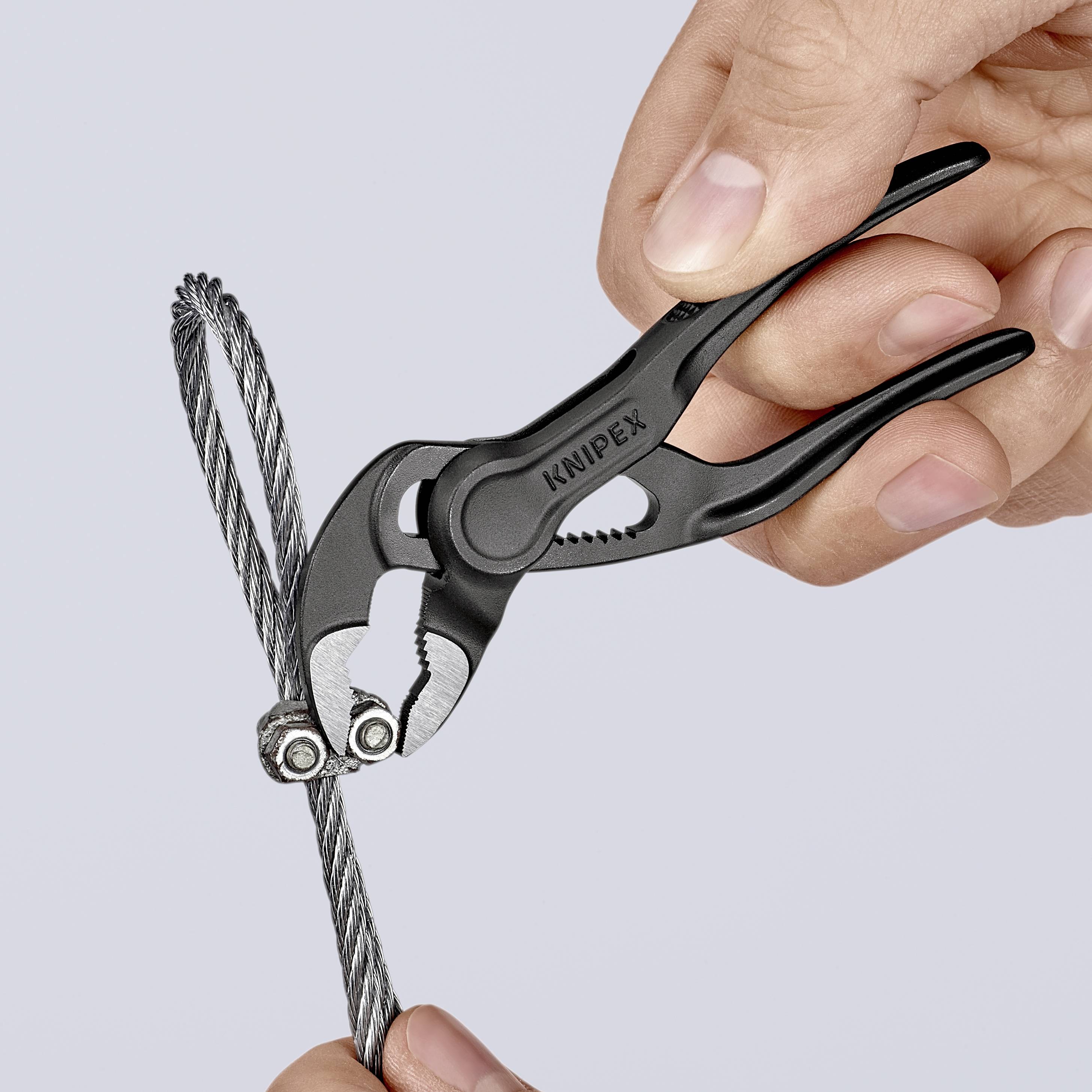 A hand is holding bolt cutters poised to cut through a steel cable. The tool is precisely positioned.