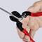 A hand is holding a red pair of pliers cutting through a silver wire rope. The pliers are marked with 'KNIPEX' and the model number.