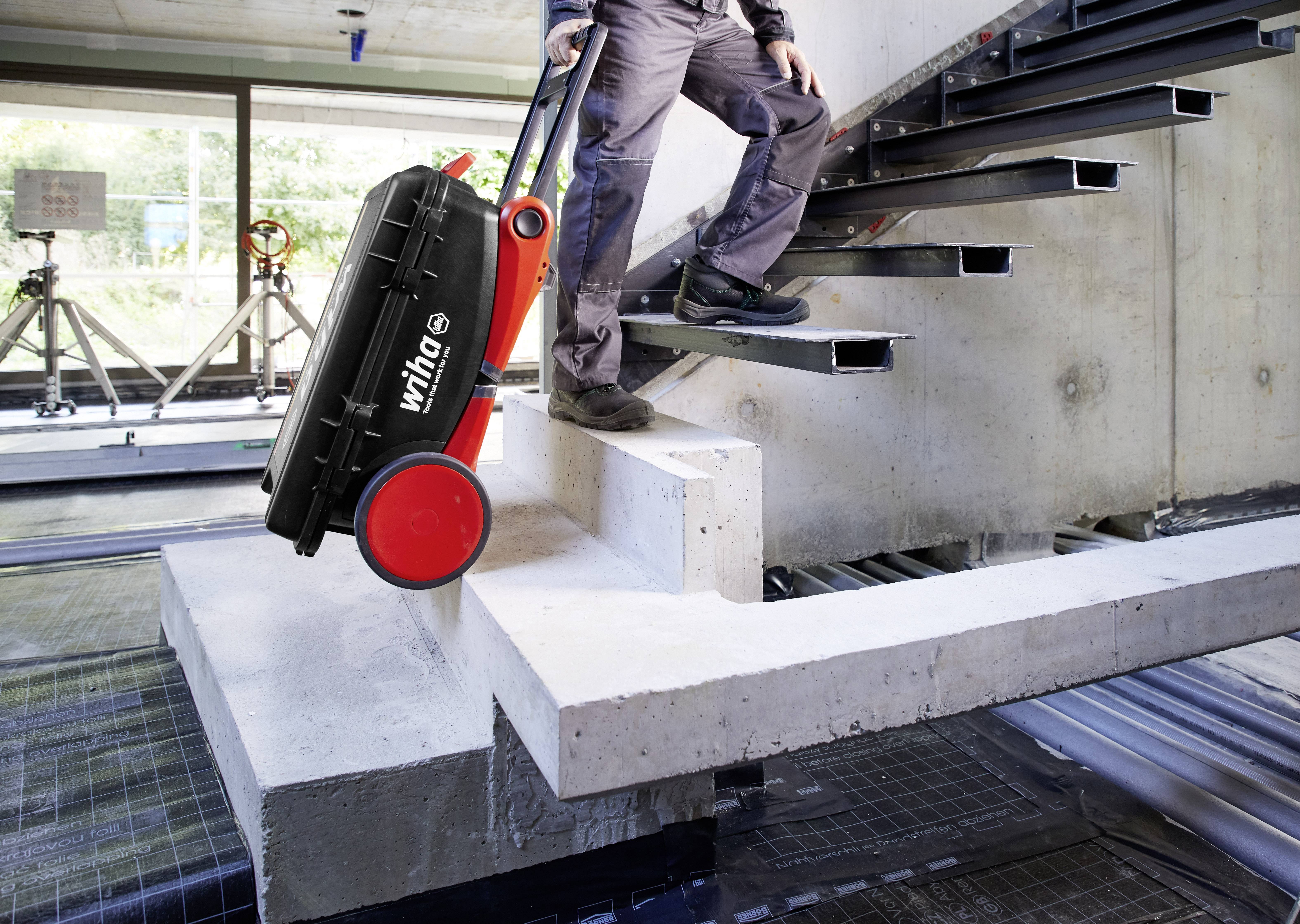 A person is transporting a toolbox down a staircase using a sack barrow in a construction site environment.