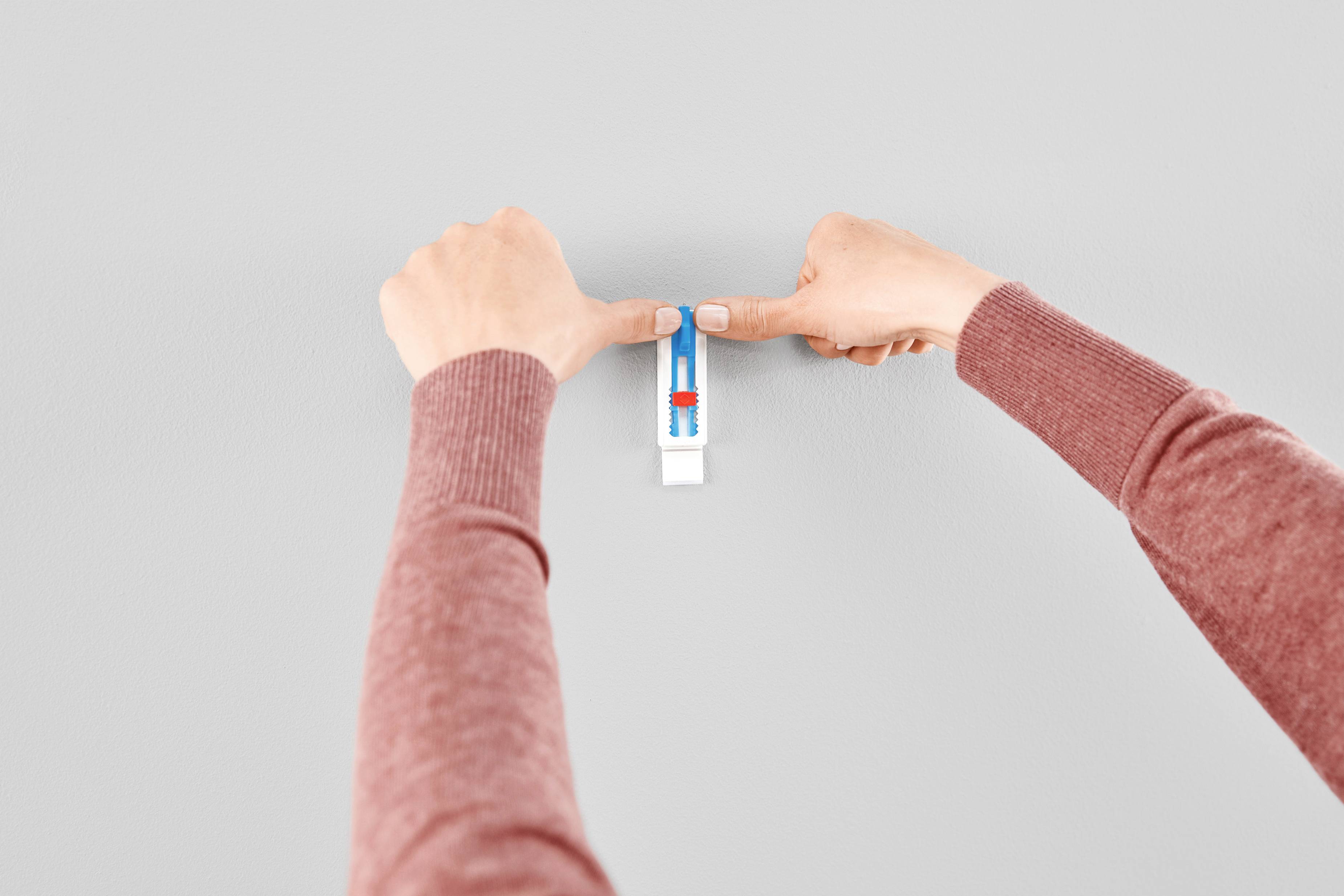 Two hands are attaching a rectangular spirit level to a grey wall.