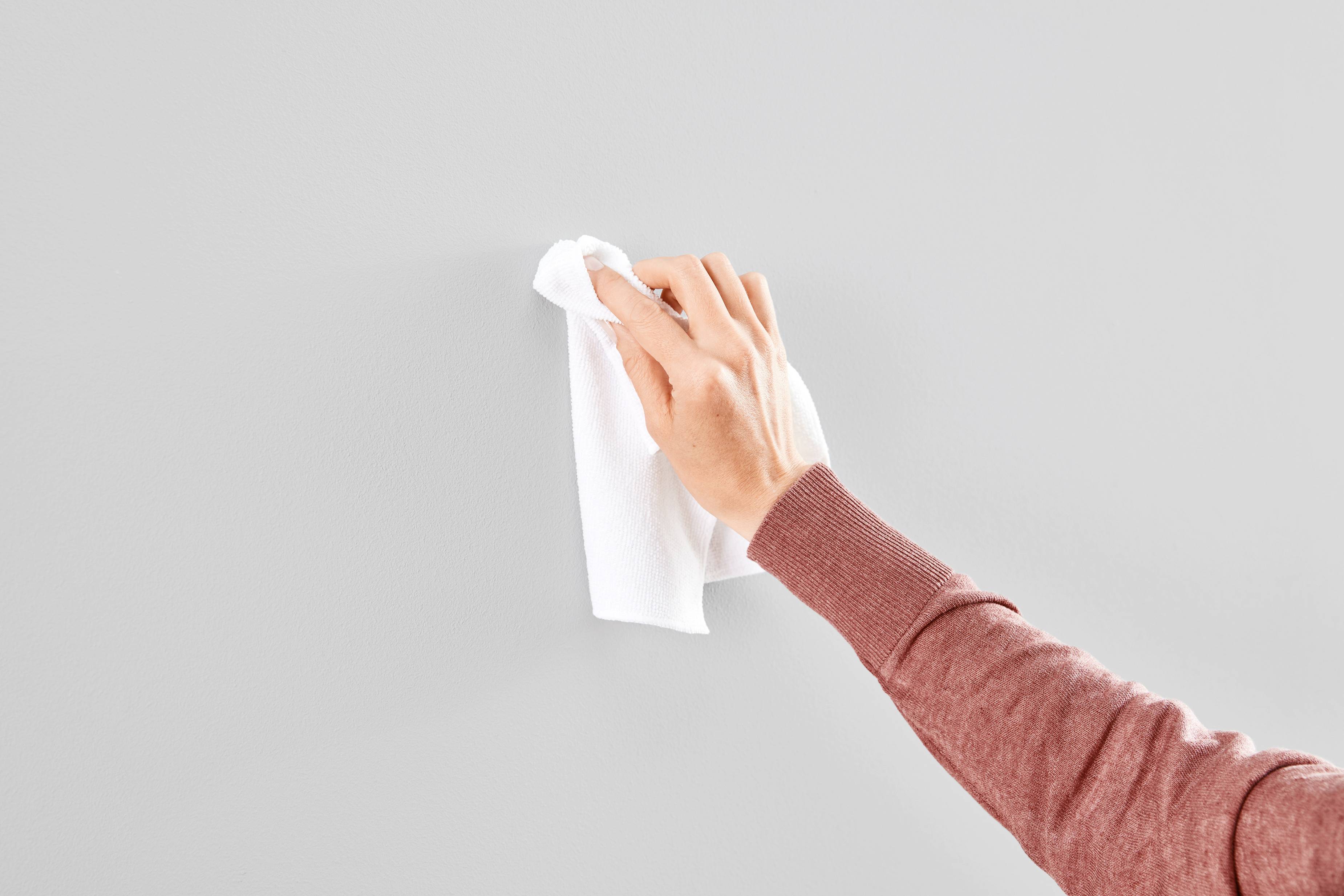 A hand wipes a grey wall with a white cloth.