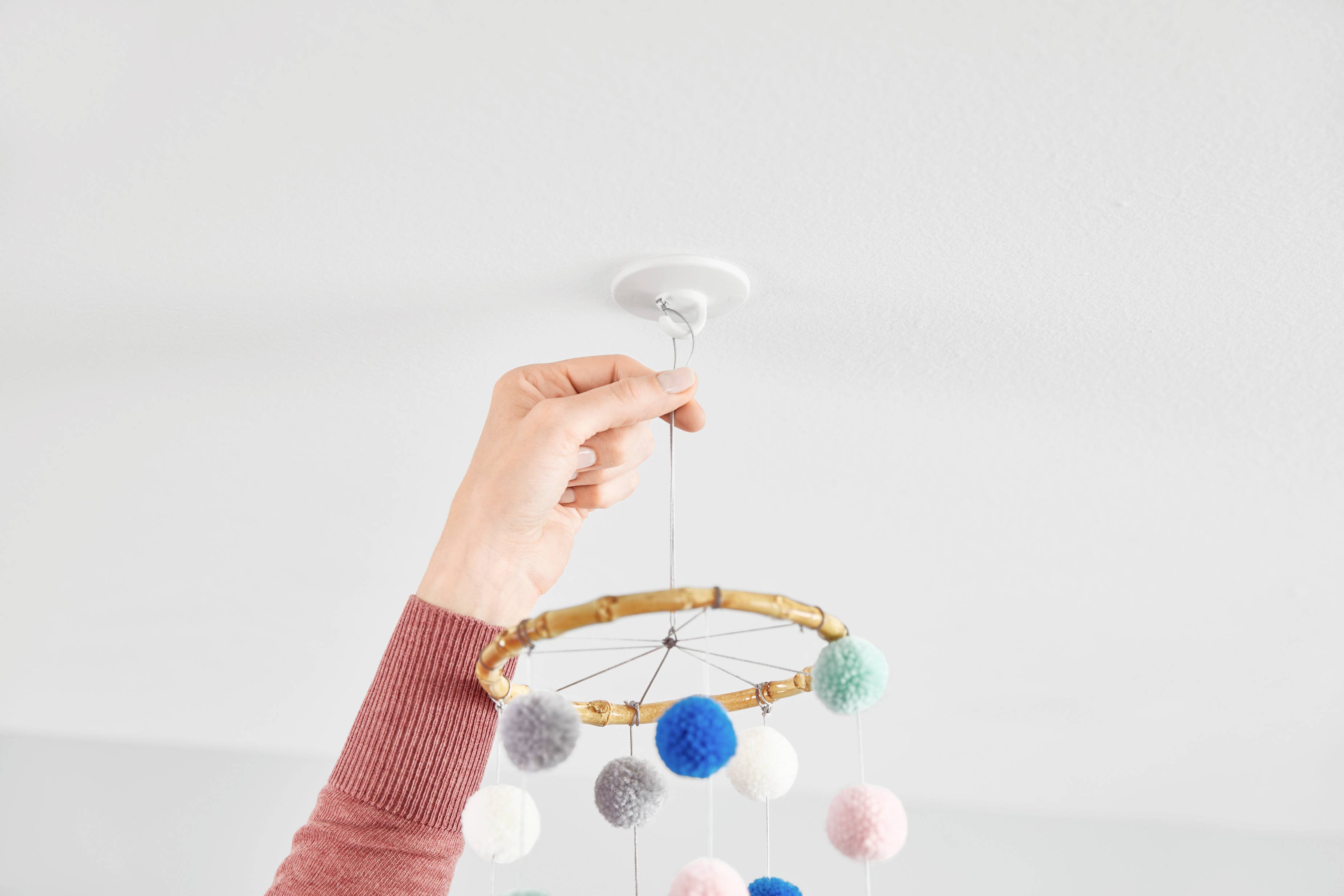 'A hand attaches a mobile with colourful pompoms to the ceiling.'
