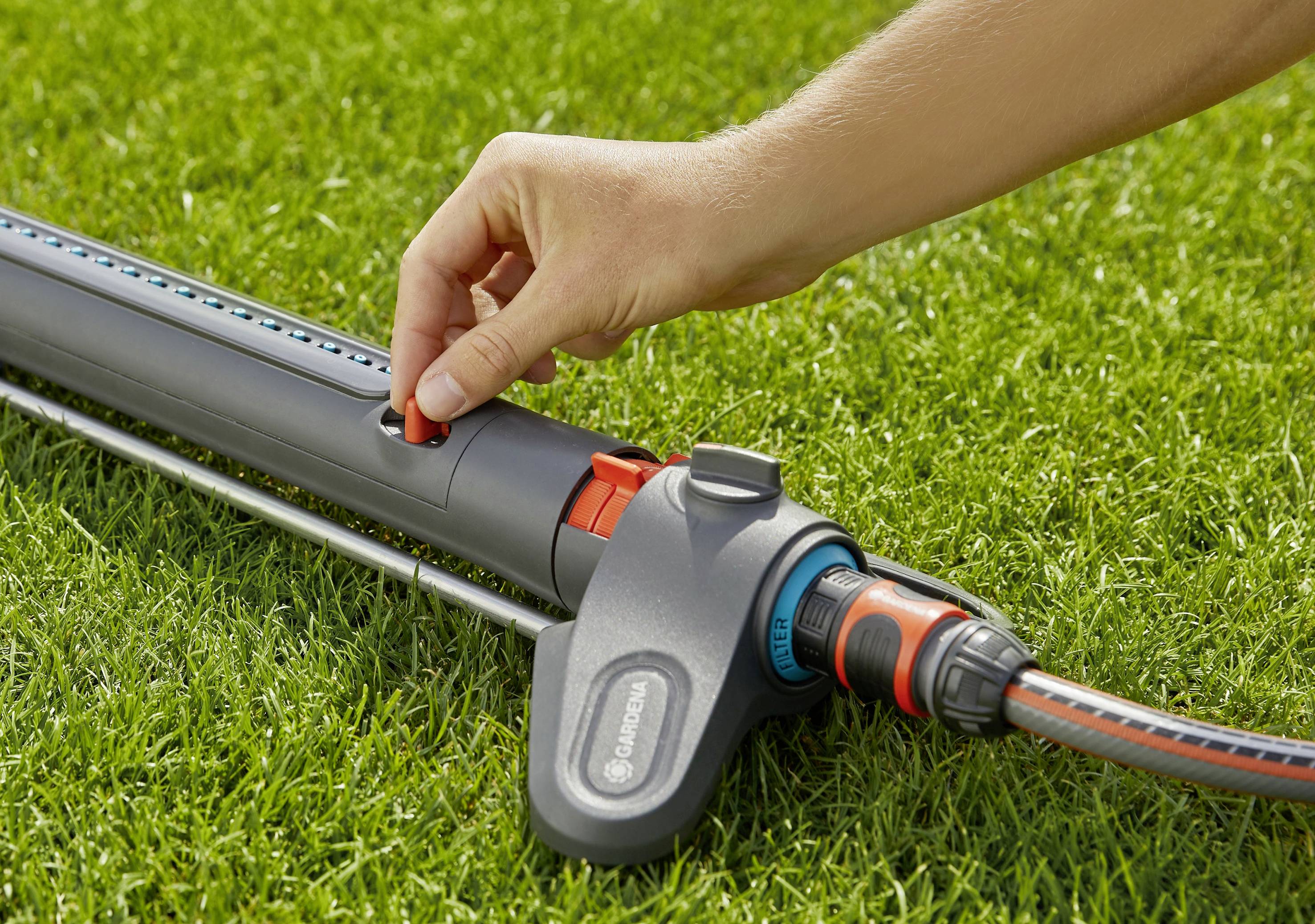 A hand is positioning a lawn sprinkler on a green lawn. The sprinkler is connected to a hosepipe.
