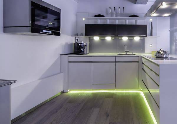 Modern kitchen with white cupboards, built-in oven, coffee machine and LED lights underneath the cupboards and along the floor.