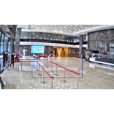Entrance area of a modern building with a reception desk on the right. On the left, barrier tapes and people wearing masks are visible.