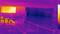 A thermal image shows an interior space with barriers in the foreground and a large bright screen on the left. The colour palette ranges from violet to yellow.