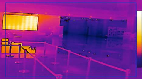 Thermal image of a hall with barriers in the foreground. Bright areas indicate heat sources, while darker areas are cooler.