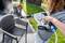 A person is spraying water with a handheld device onto a plastic chair in the garden, with flowers in the background.