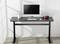 A black desk with a computer, keyboard and mouse. Next to it stands a mug with pens and red headphones. Background: white room.