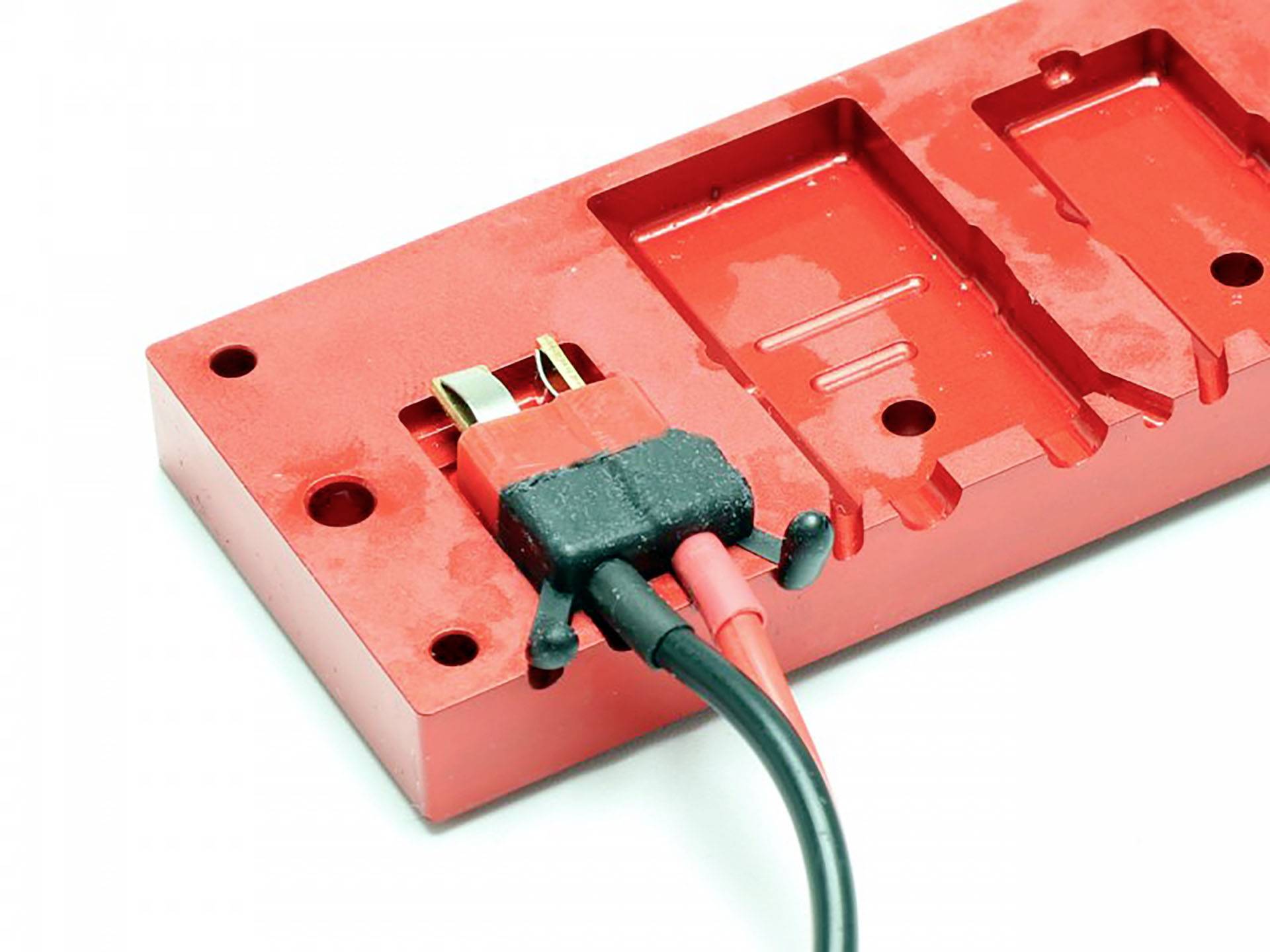 Red plug system connected with two cables to a rectangular module used for industrial or technical applications.