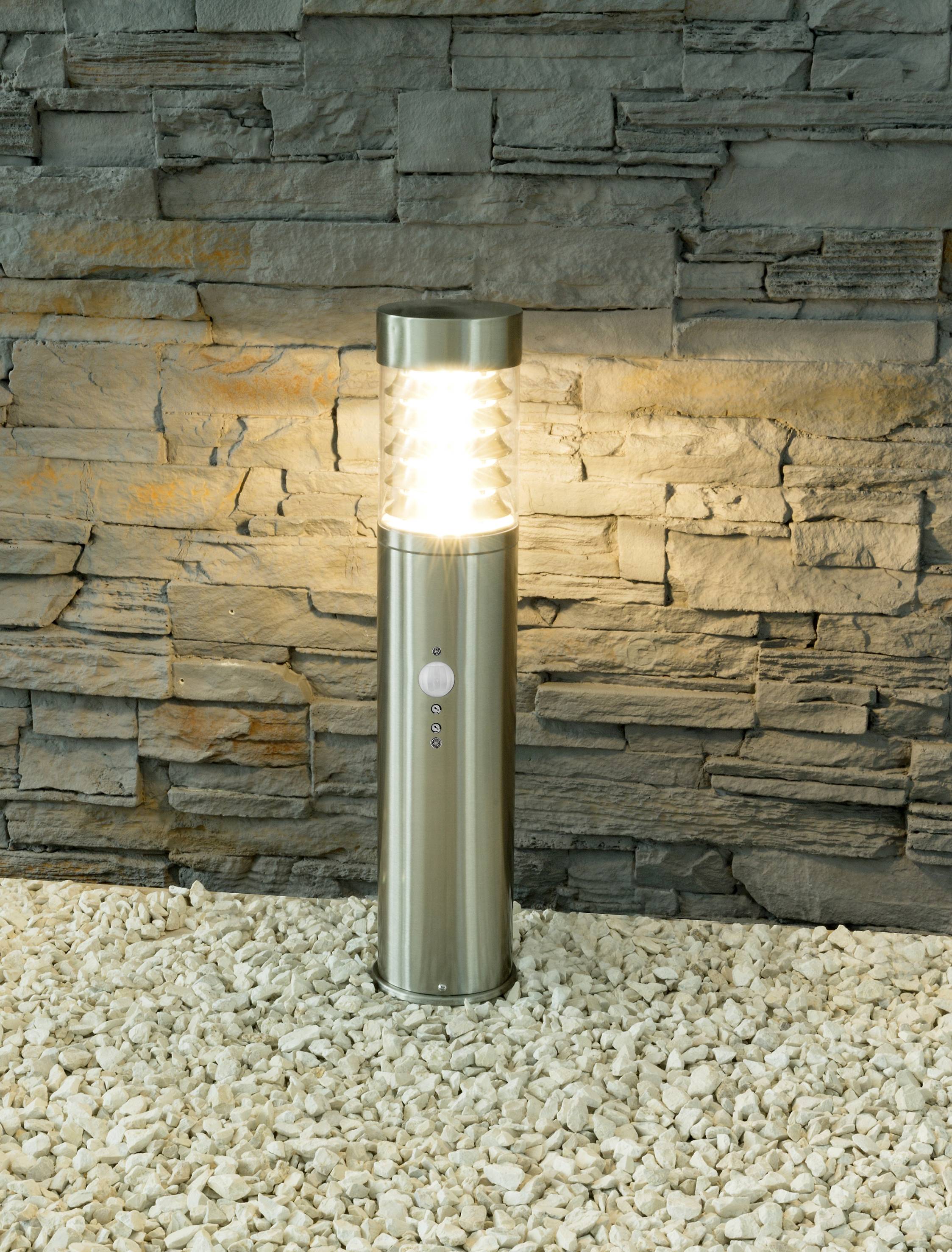 A silver exterior light on white gravel shines against a stone wall.