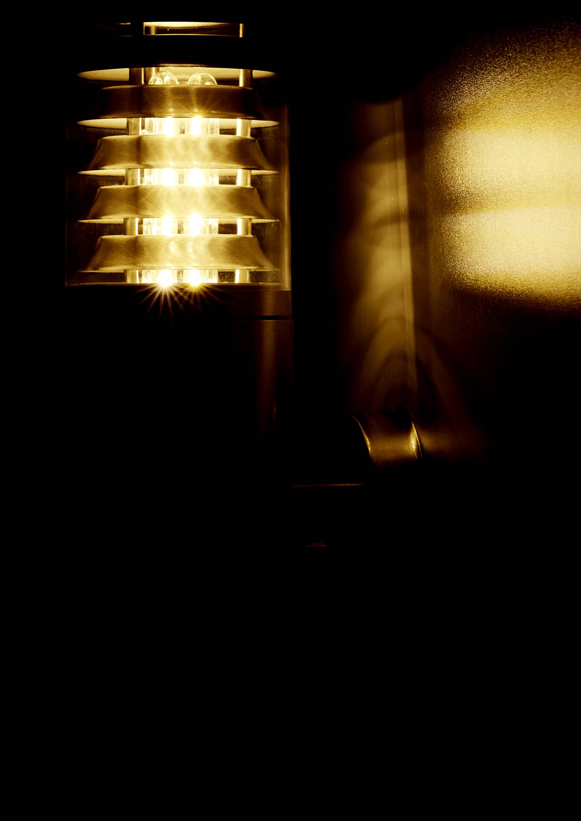 A wall light that emits warm, yellow light through louvres, casting patterns on the wall and creating a cosy atmosphere.