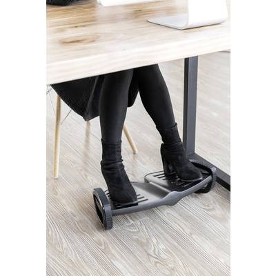 A person is sitting at a desk and using a footrest with wheels. The person is wearing black boots and black clothing.