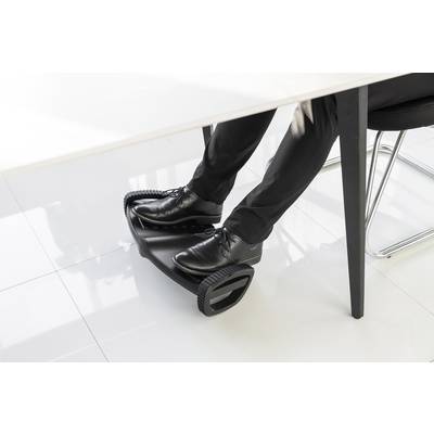 A man in a suit sits at a desk, using a black footrest to improve his posture.