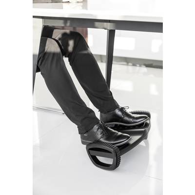 A person in black trousers and shoes is resting their feet on a black footstool underneath a table.