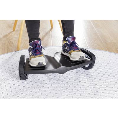 'Two feet in trainers stand on a black balance board with ridged wheels, on a light wooden floor and carpet.'