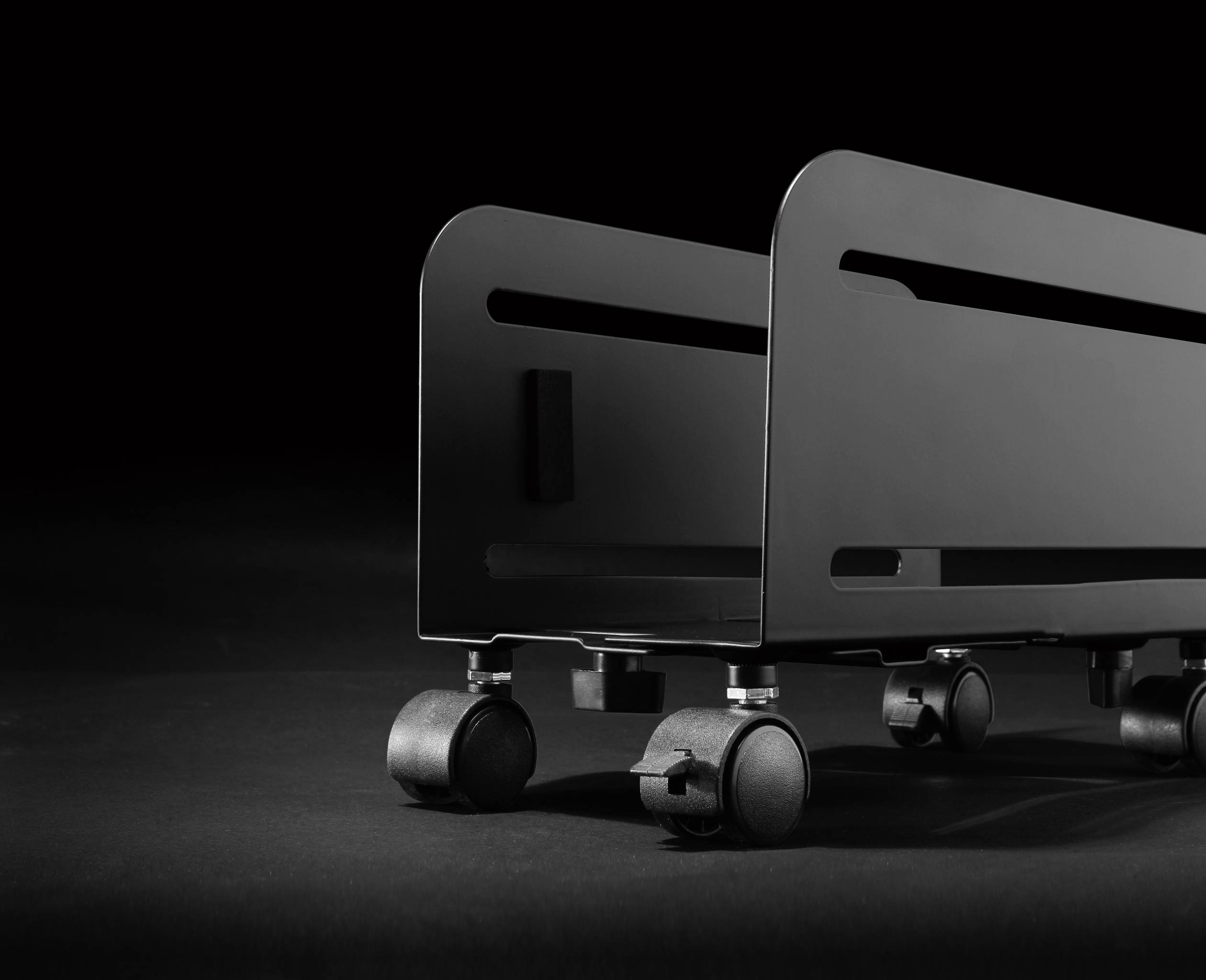 A black, minimalist wheeled storage trolley against a dark background. Design-focused, industrial style.