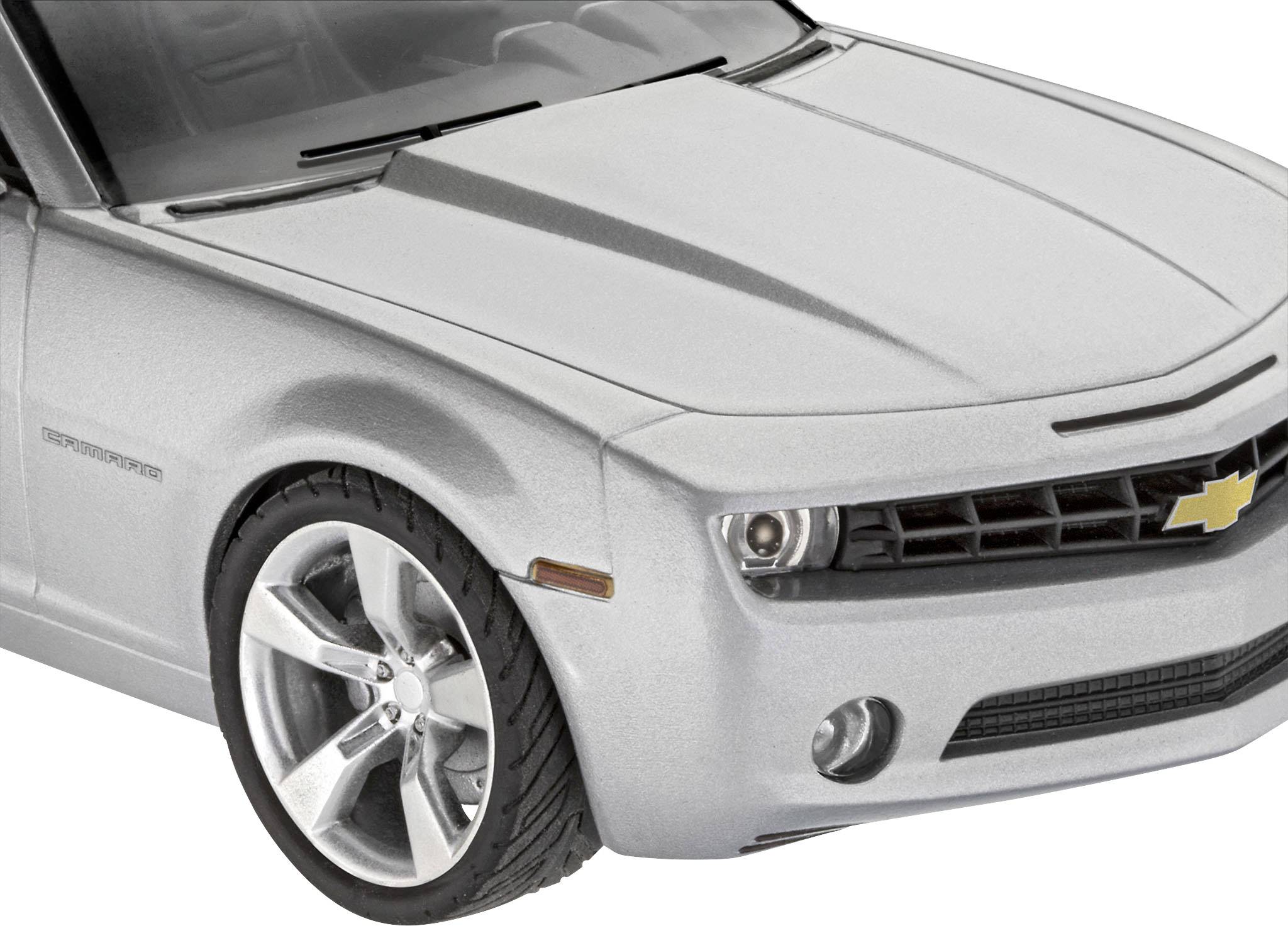A silver car in close-up shows the front wheel area and the radiator grille with a yellow emblem on the black grille.